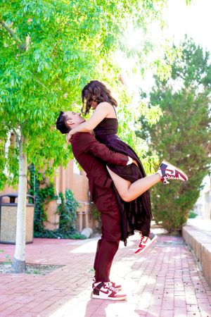 A playful couple sharing a joyous moment on a brick pathway surrounded by trees.