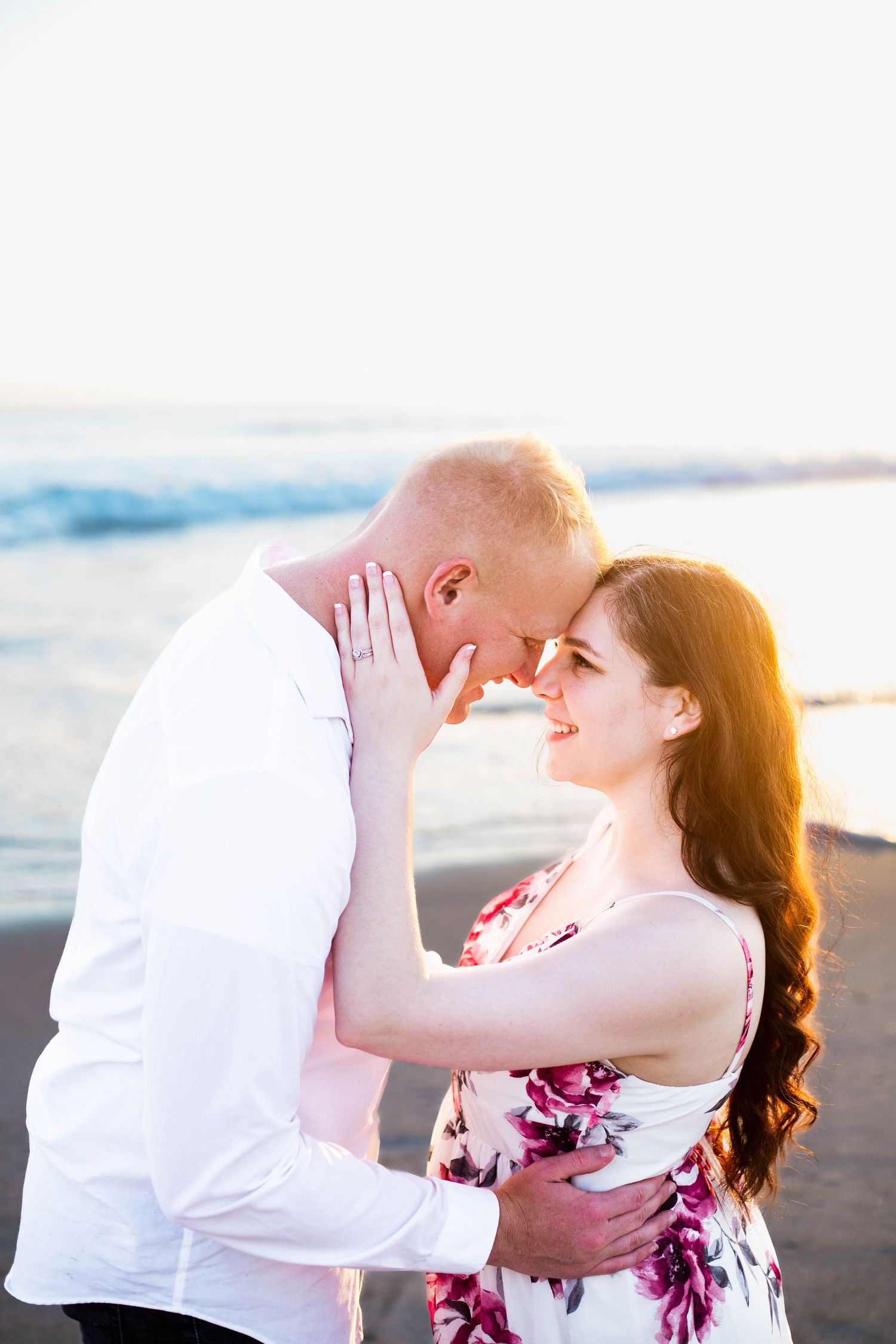 Romantic couple embracing on beach at sunset during engagement photoshoot.