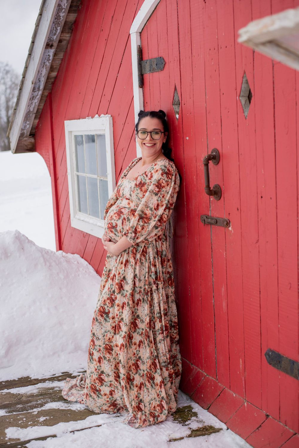 A floral maxi dress is worn against a bright red barn door surrounded by snow in winter.