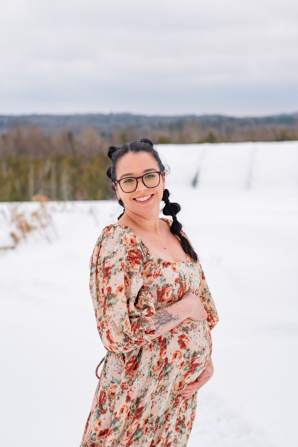 A floral dress stands out against a snowy winter landscape with rolling hills and bare trees in the background.
