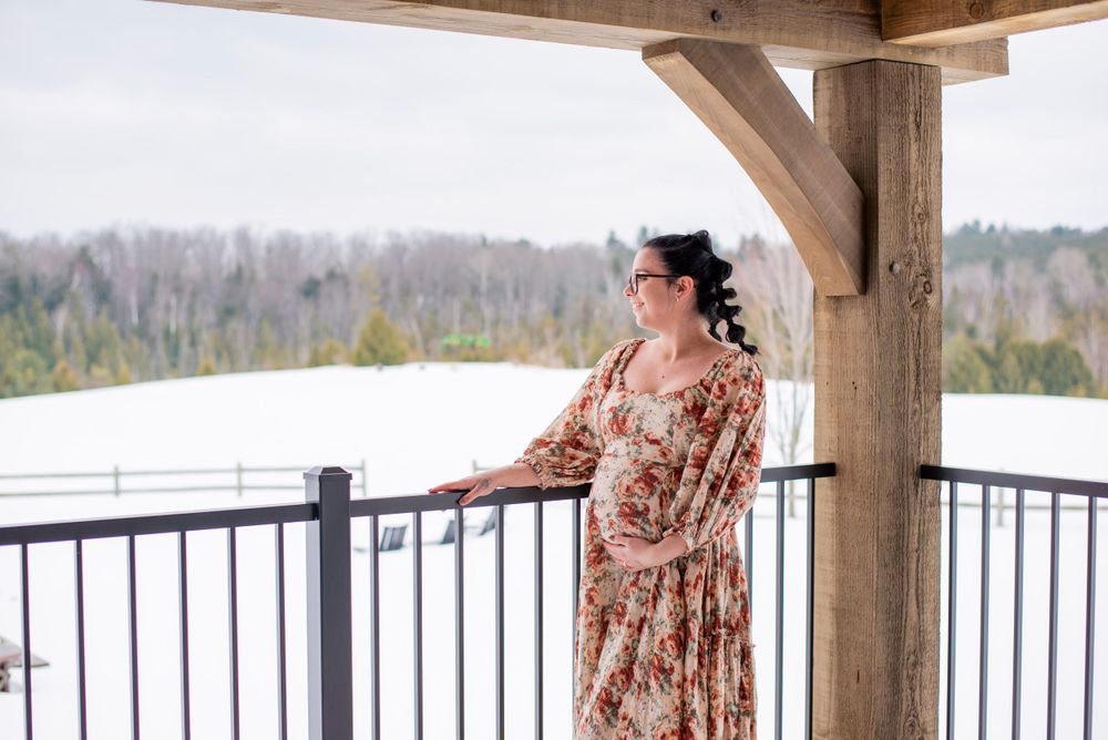 Someone in a floral dress stands on a covered deck overlooking a snowy winter landscape in the mountains.