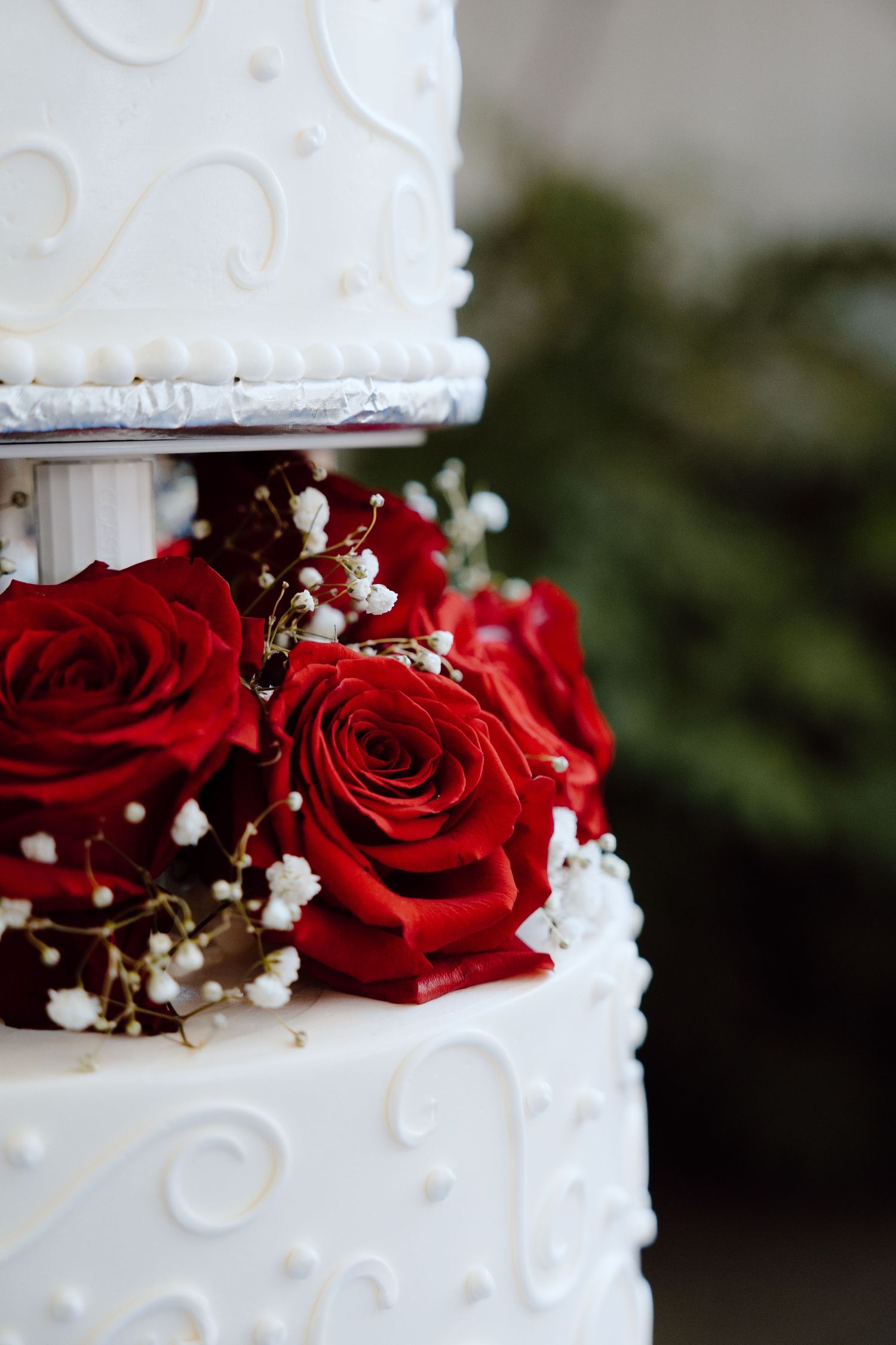 Close-up of a white wedding cake decorated with red roses and baby's breath flowers.