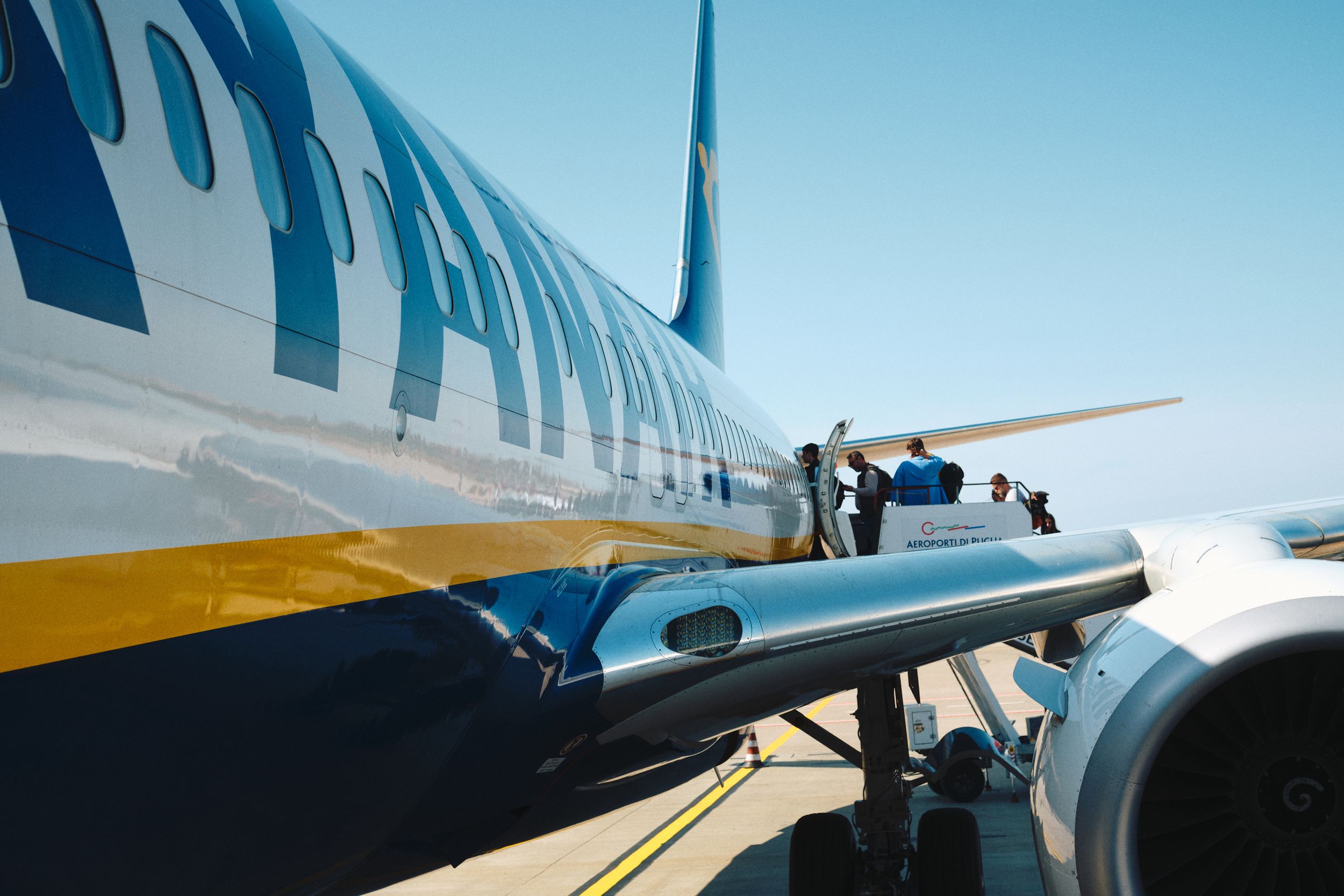 Passengers boarding a Ryanair aircraft on the tarmac under bright blue sky.