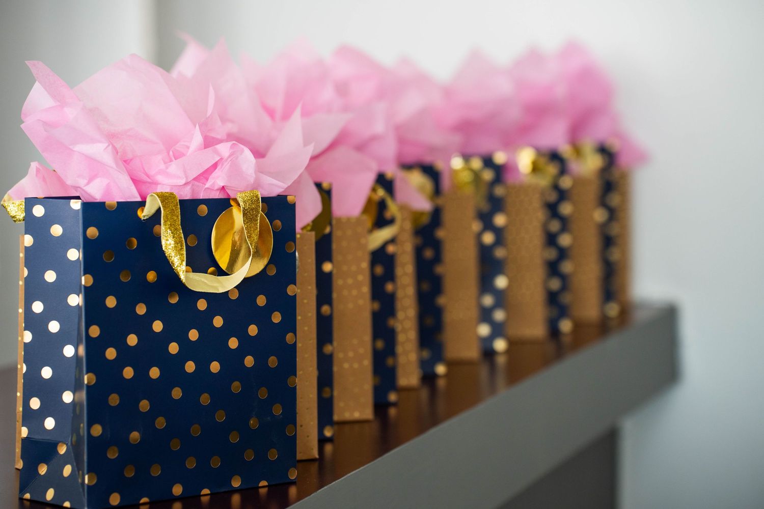 Navy and gold decorative gift bags with pink tissue paper arranged in a row.