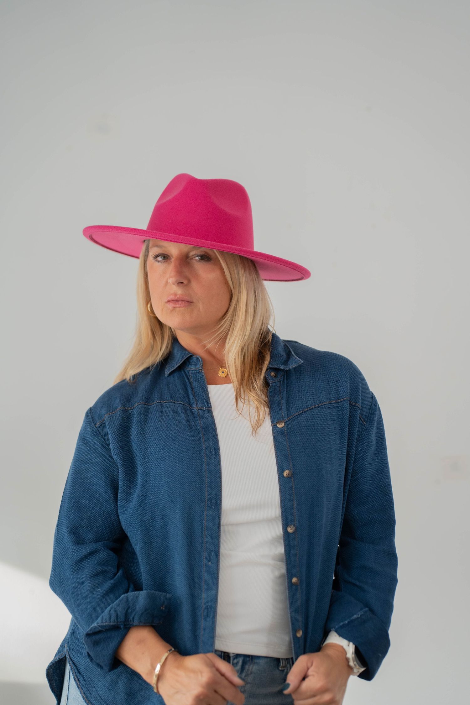 Woman wearing denim jacket and bright pink hat poses against white background.