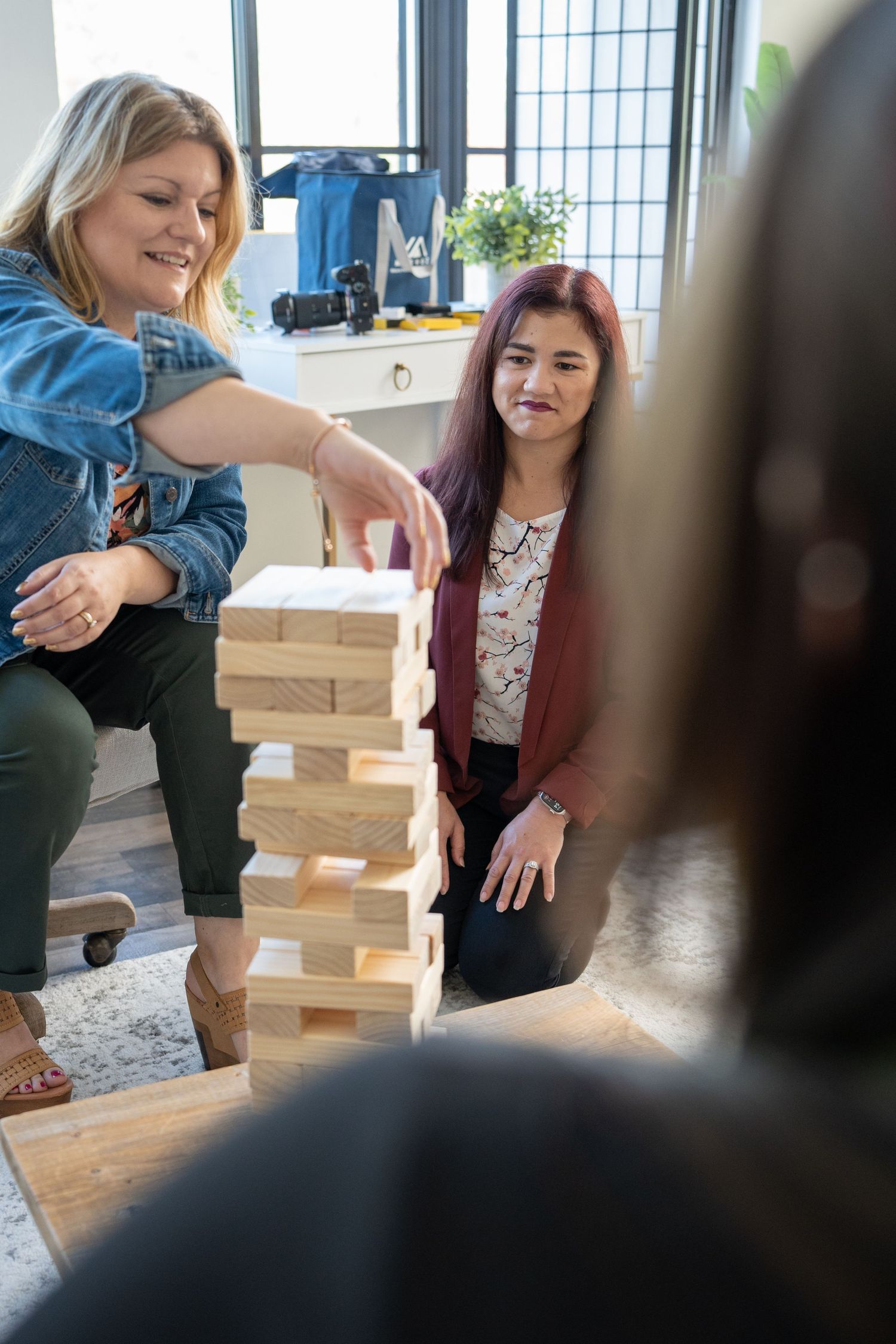 Friends playing Jenga together in a well-lit room with large windows.