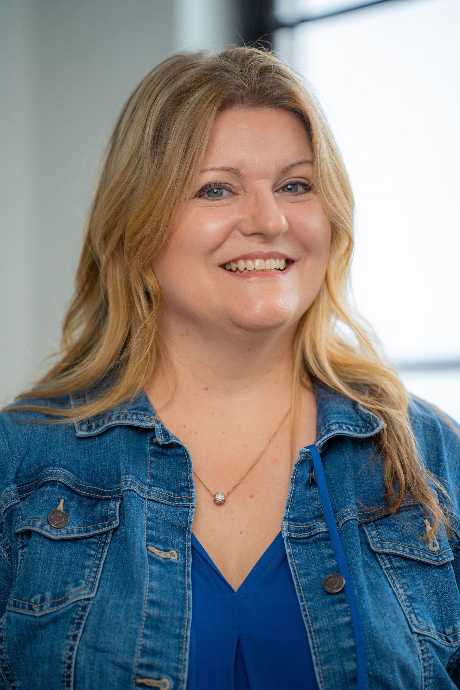 Woman in denim jacket and blue top smiling warmly in professional headshot.