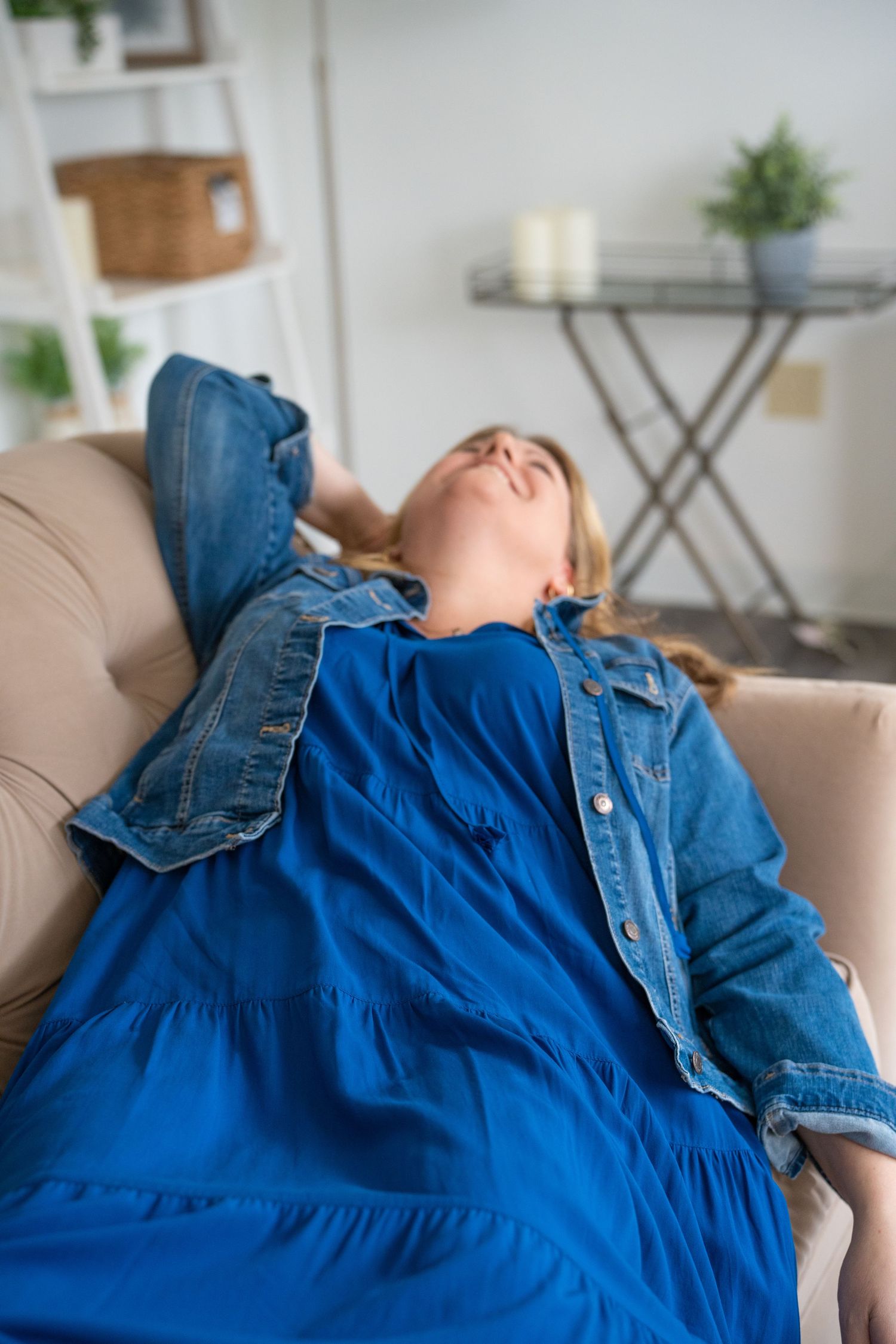Someone wearing a blue denim dress lying back on a beige couch.