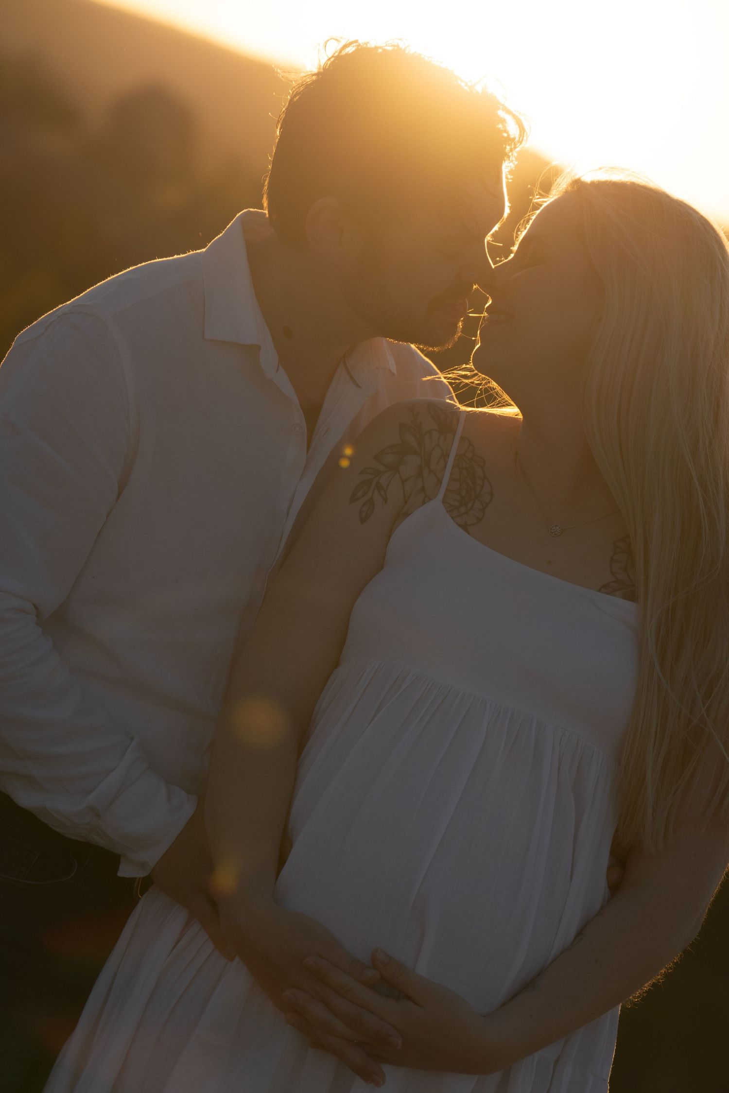 Silhouetted couple embracing tenderly during sunset with light streaming through creating a romantic atmosphere.