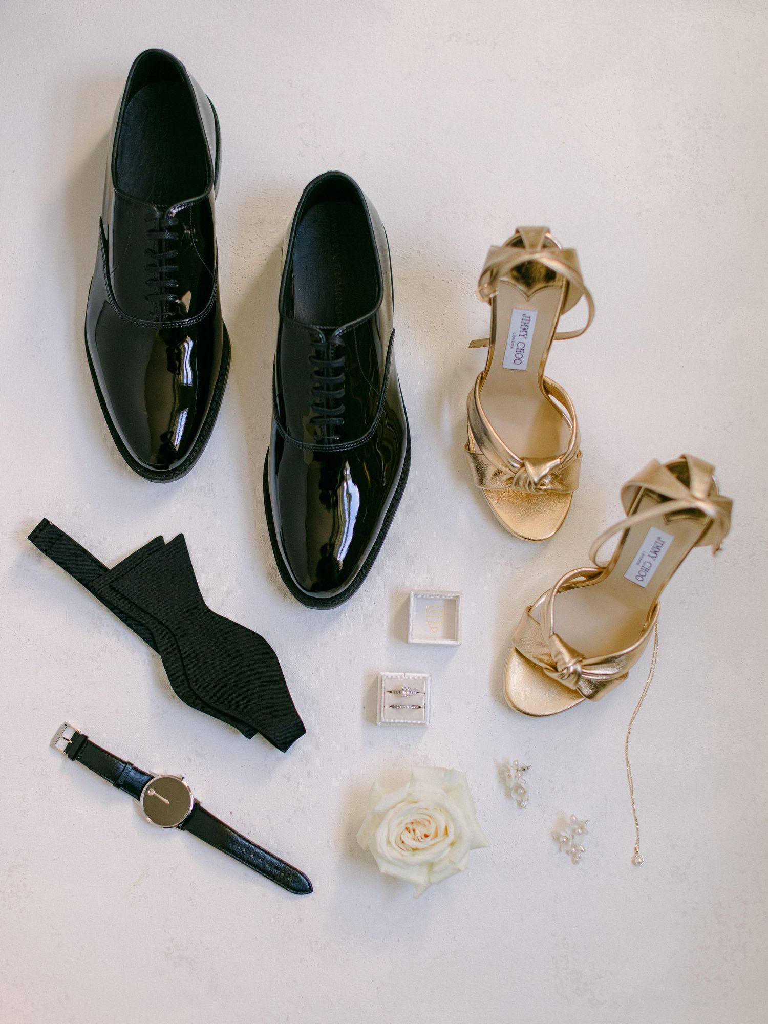 Wedding accessories including patent leather shoes, gold sandals, bowtie, watch and white rose.
