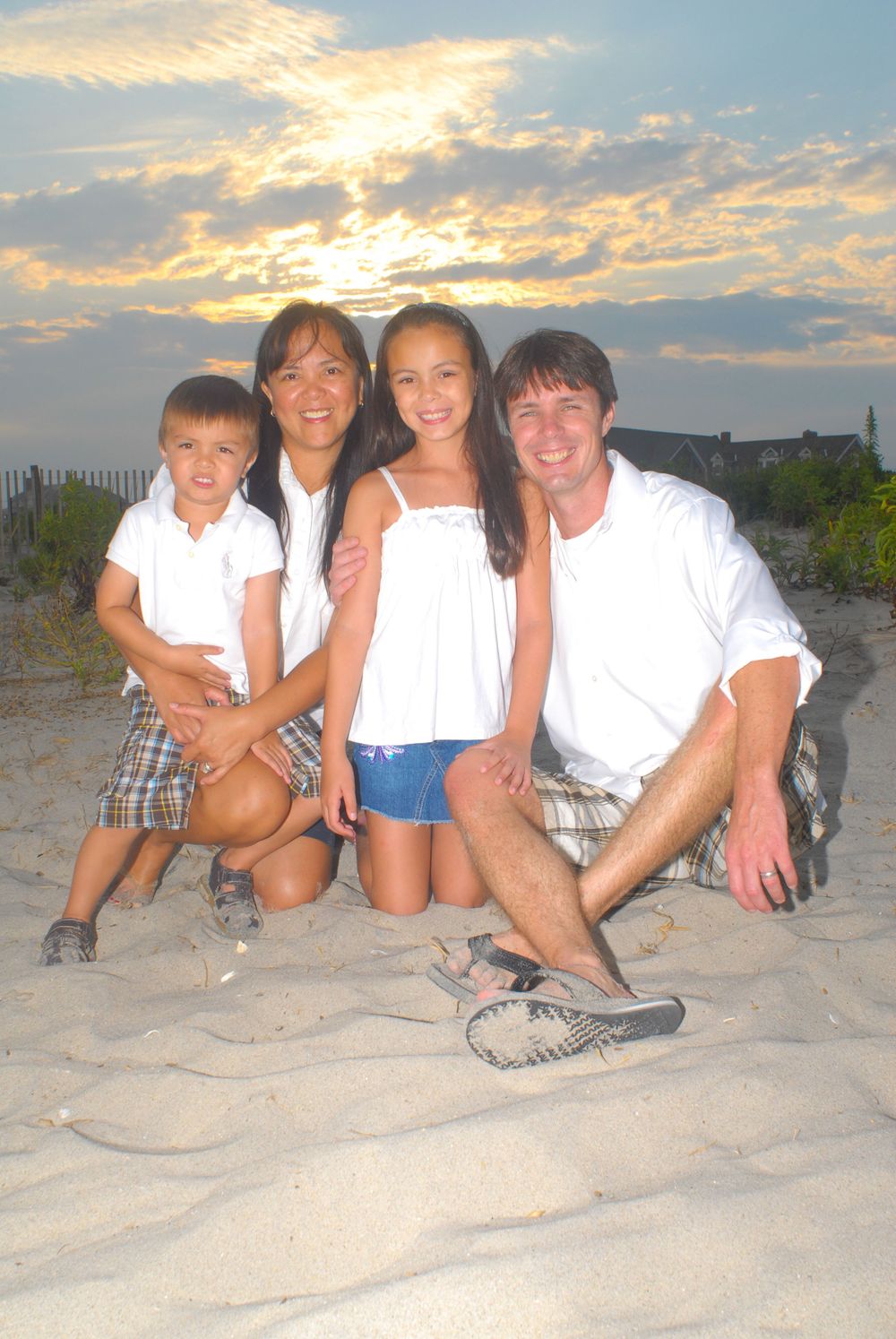 A family group poses together on a sandy beach at sunset.