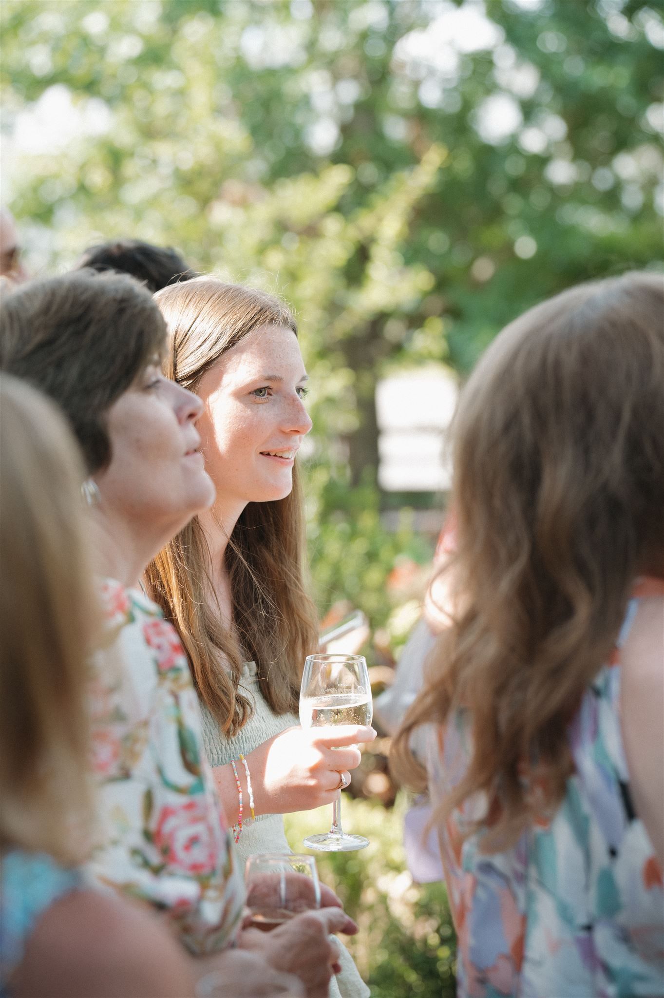 A group of friends enjoying wine glasses outdoors on a sunny afternoon in a garden setting.