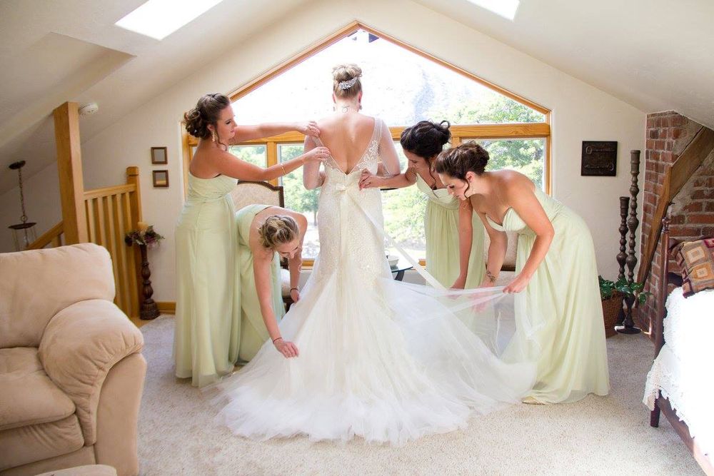 Bridesmaids in pale yellow dresses help adjust bride's wedding gown in sunlit room.
Wedding photography