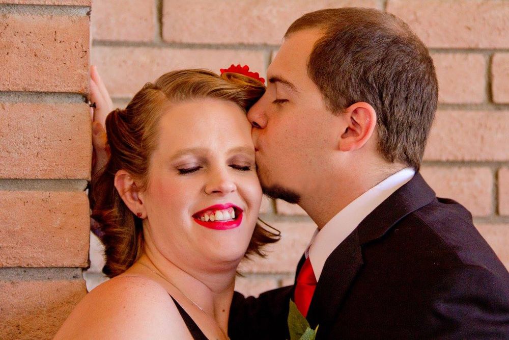 Romantic moment captured against brick wall backdrop with red floral accents.
Wedding photography