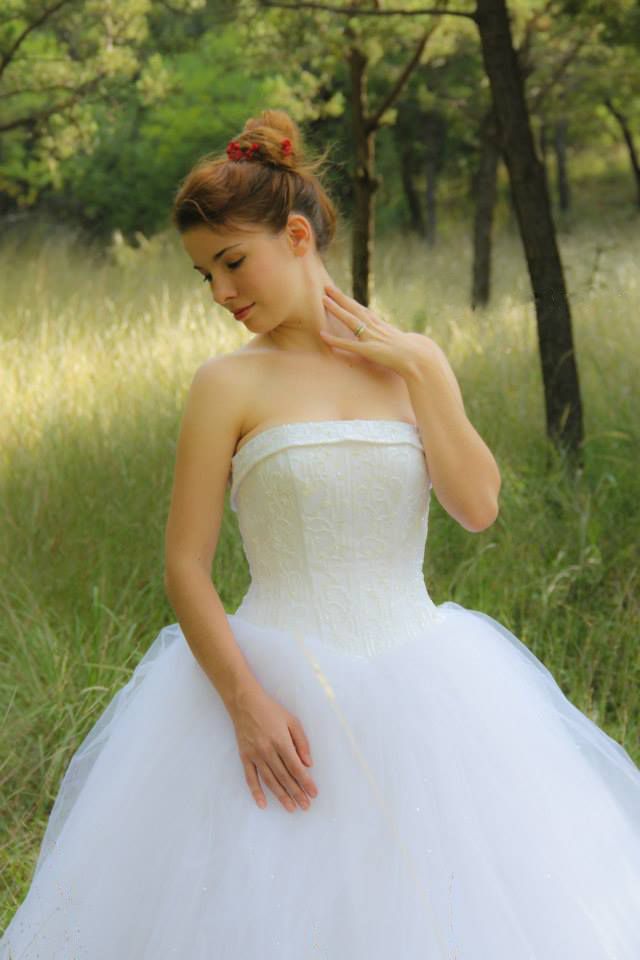 Bride in white ballgown poses gracefully in sunlit meadow with trees.
Wedding photography