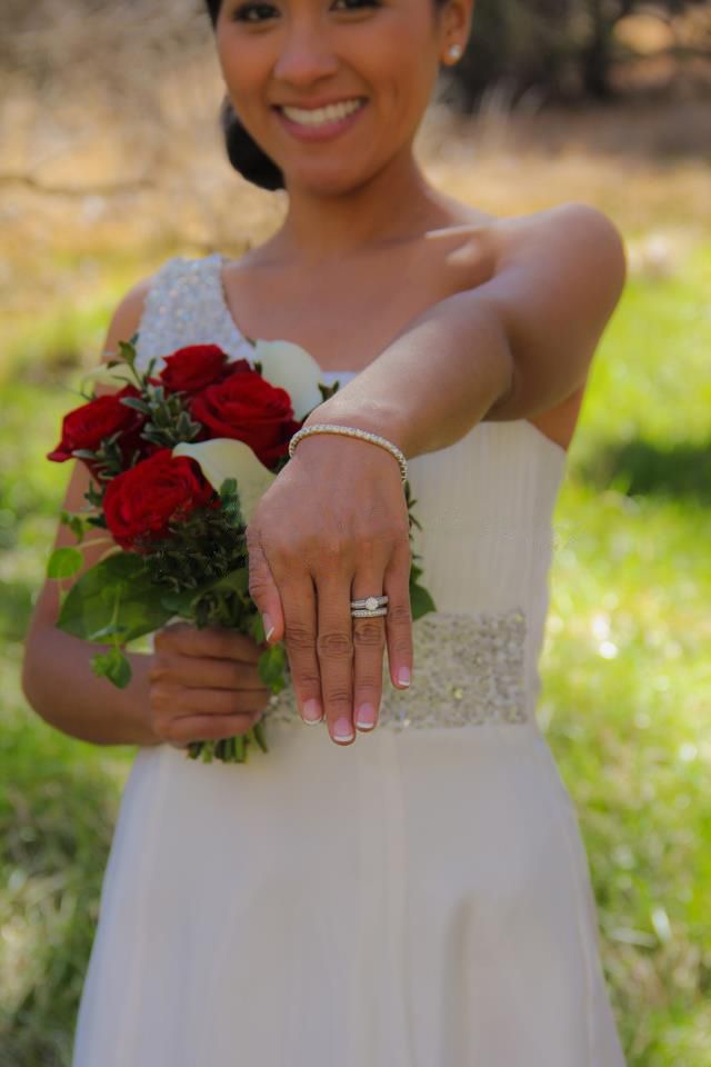 Bride in white dress showing engagement ring while holding red rose bouquet.
Wedding photography