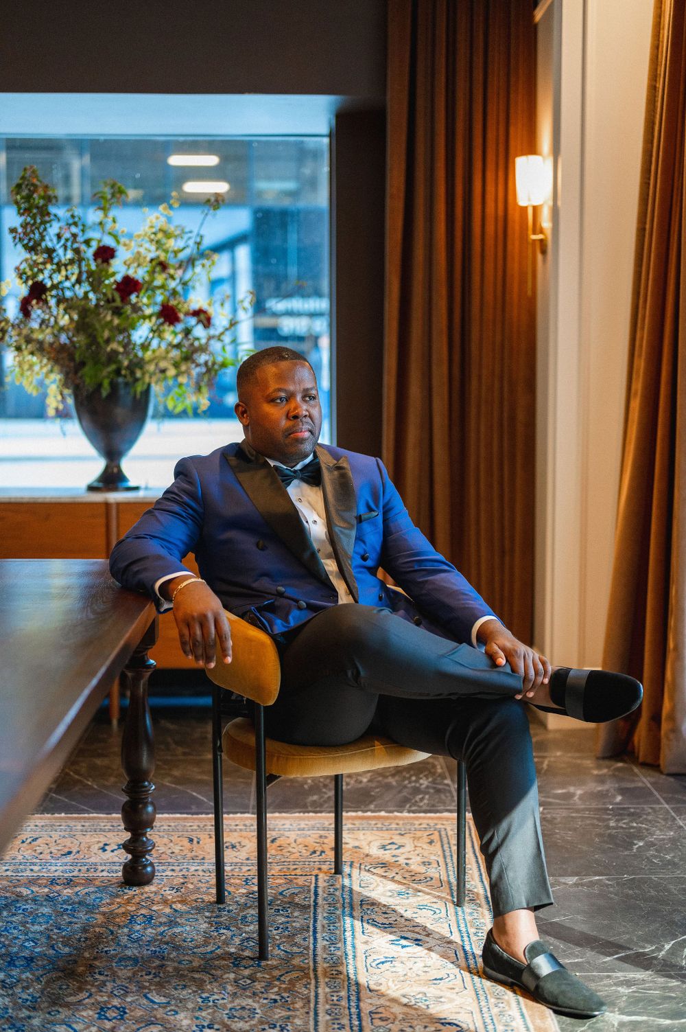 Formal attire wearing person seated elegantly in decorated interior setting.