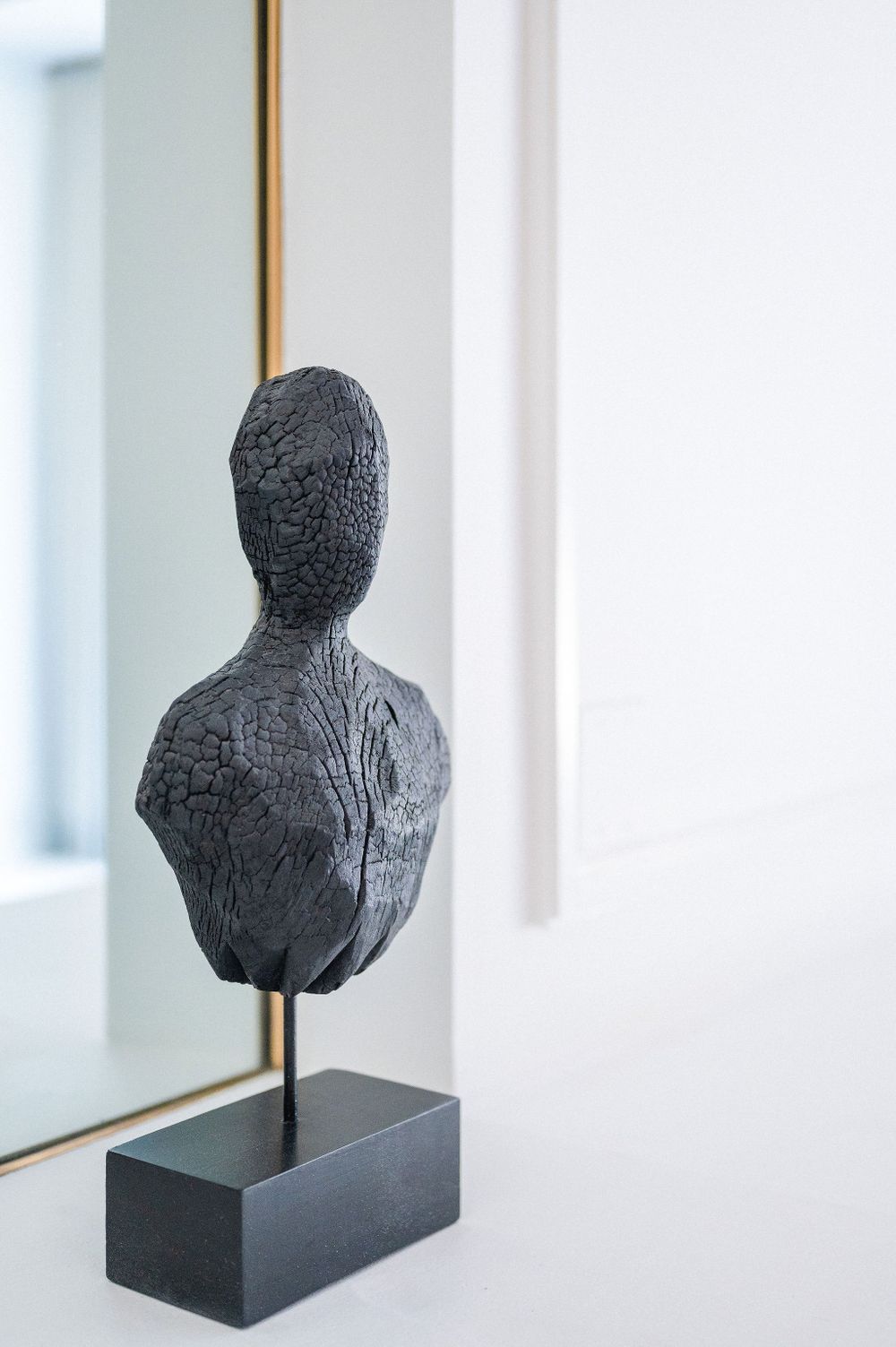 A black sculptural bust mounted on a dark pedestal against a white wall.