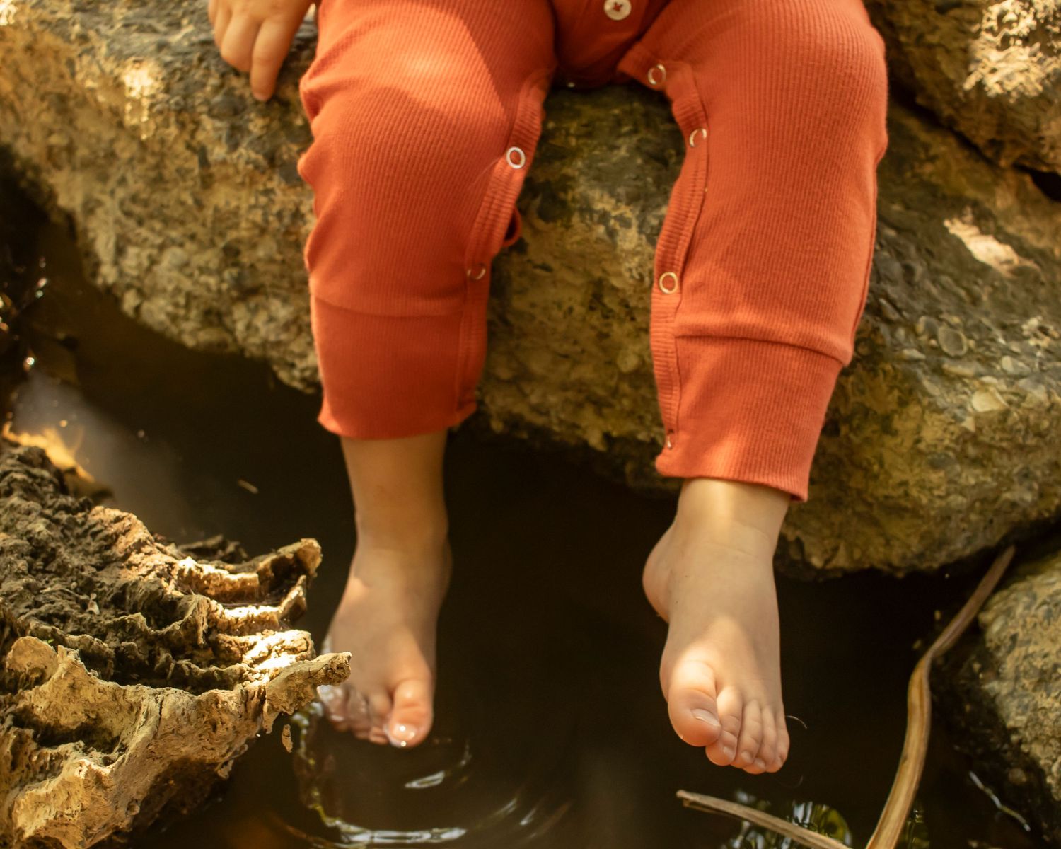 A child's feet dangle dipping into a creek