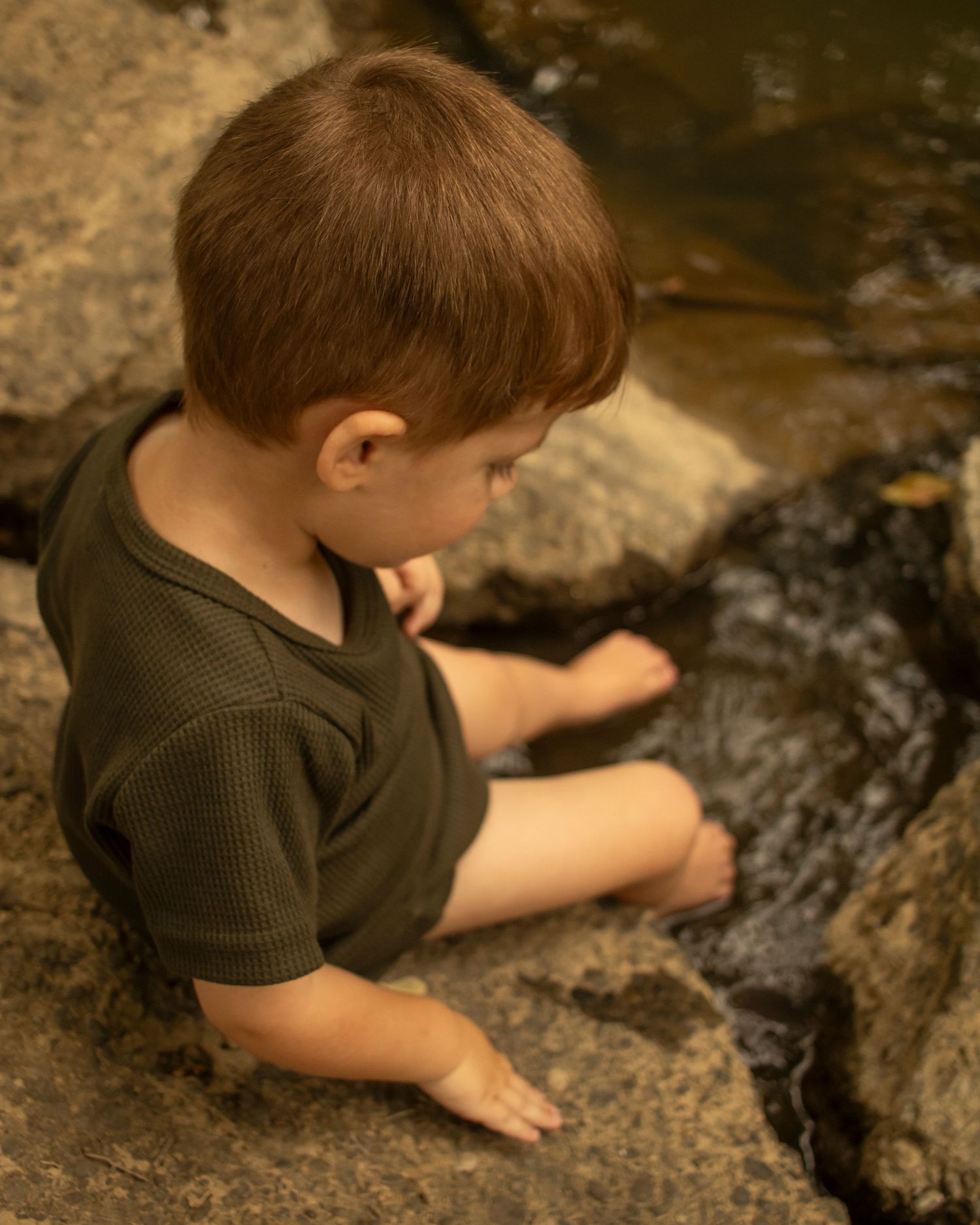 A young boy kicks his feet in a creek.