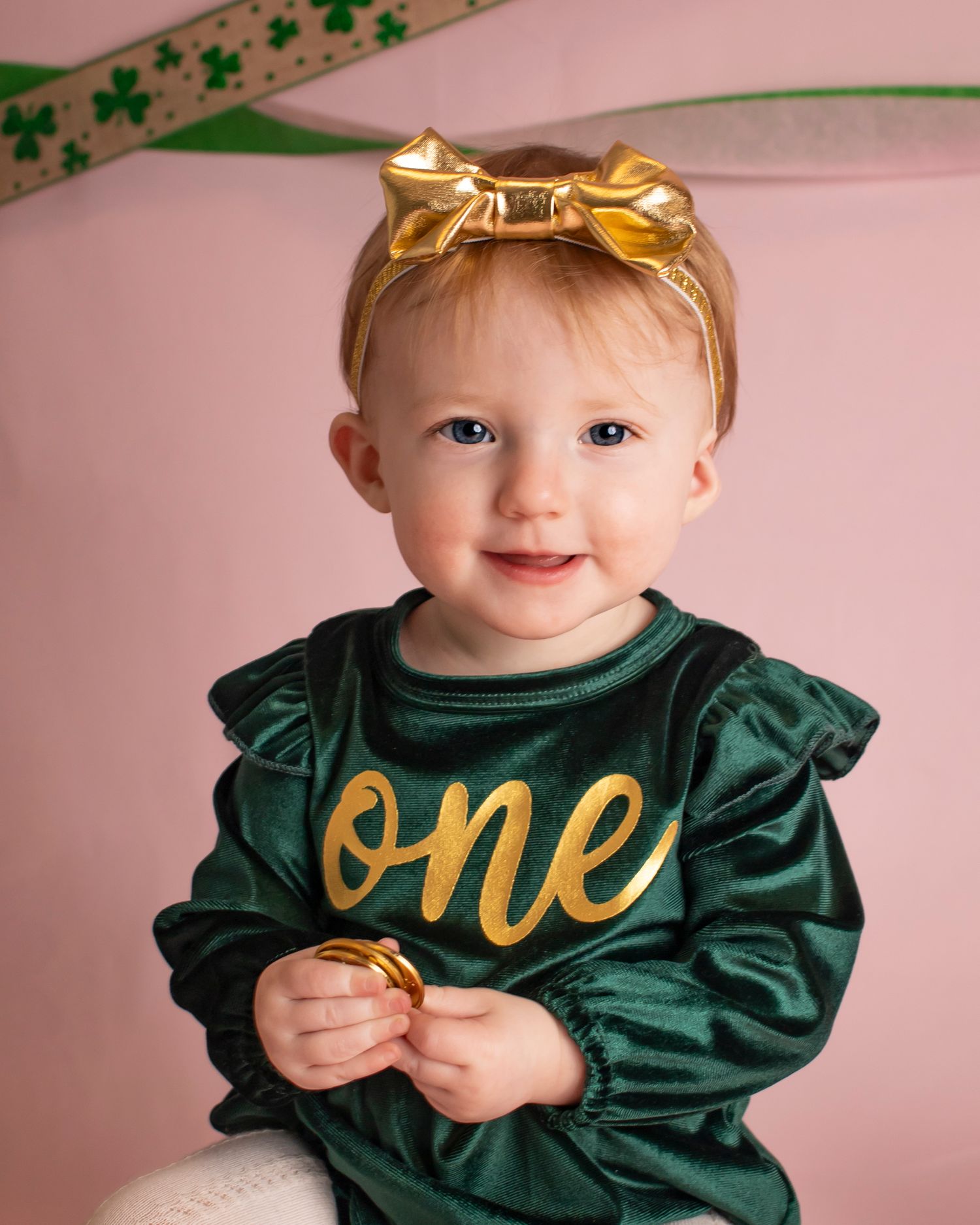 A young girl in a "one" romper smiles at the camera