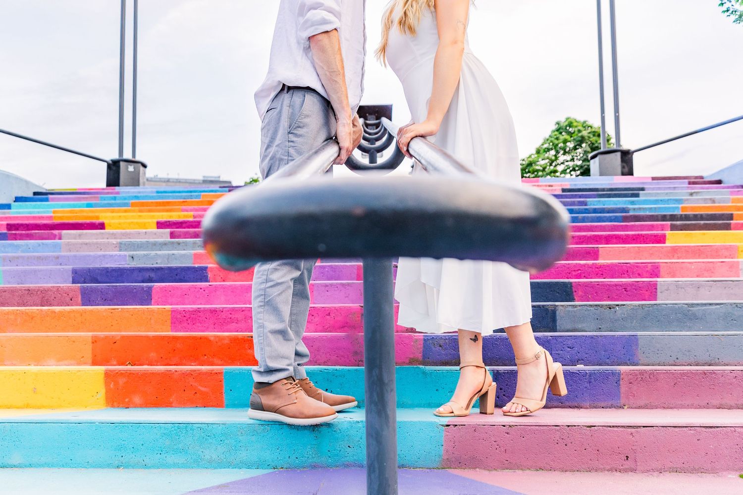 Close-up of feet on vibrant rainbow-colored stairs with black metal railing.