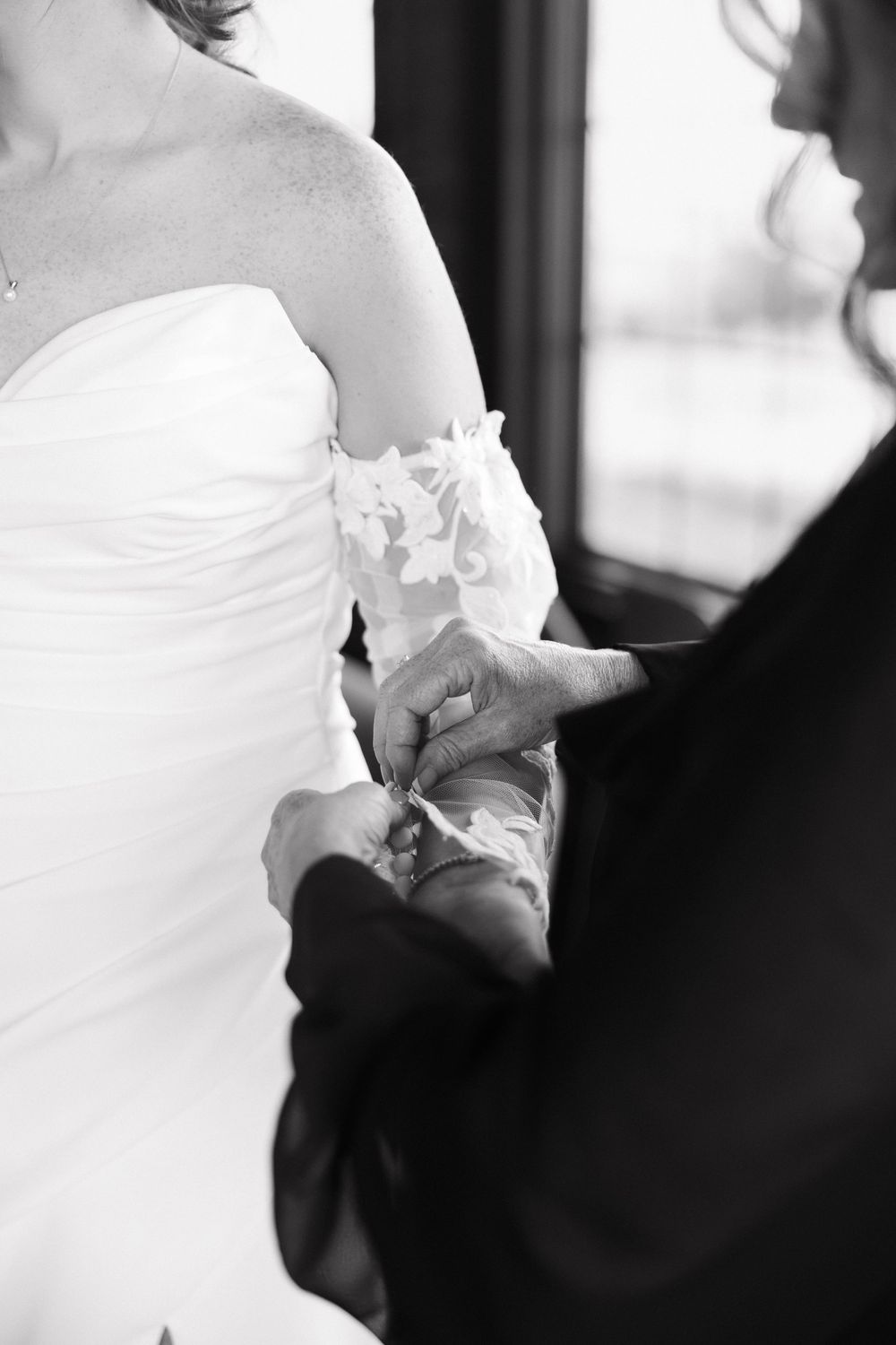 Black and white wedding photo showing close-up details of a bride's white dress and groom's dark suit.