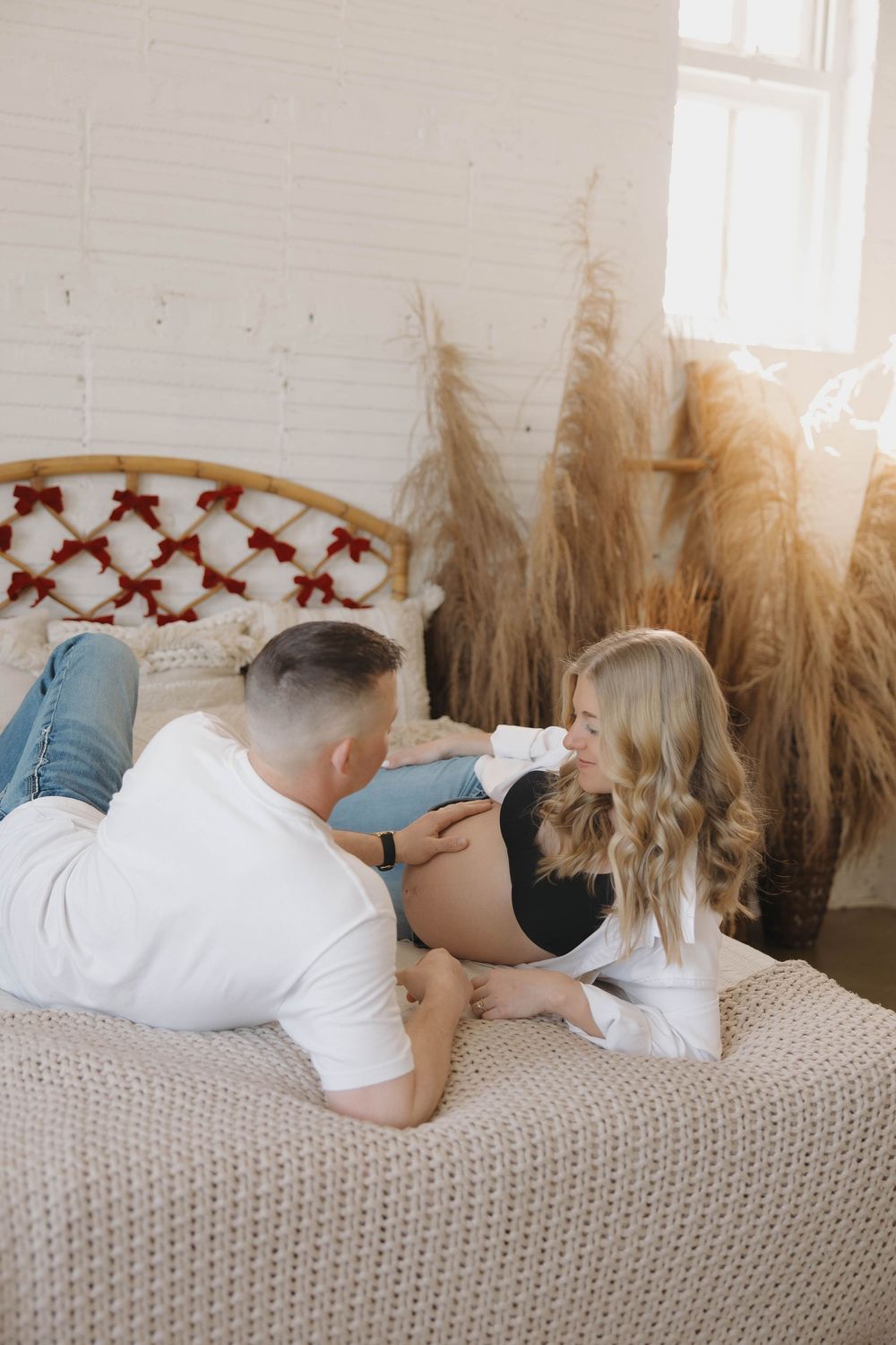 Couple lying together on a knit blanket with dried pampas grass decorations in the background.