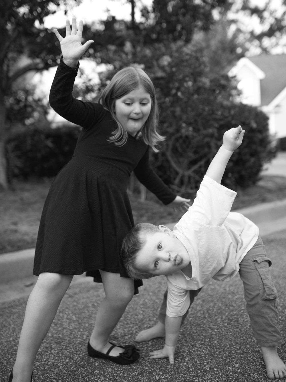 A joyful black and white photograph by B. Logsdon Photo of playful siblings on a sidewalk outdoors.