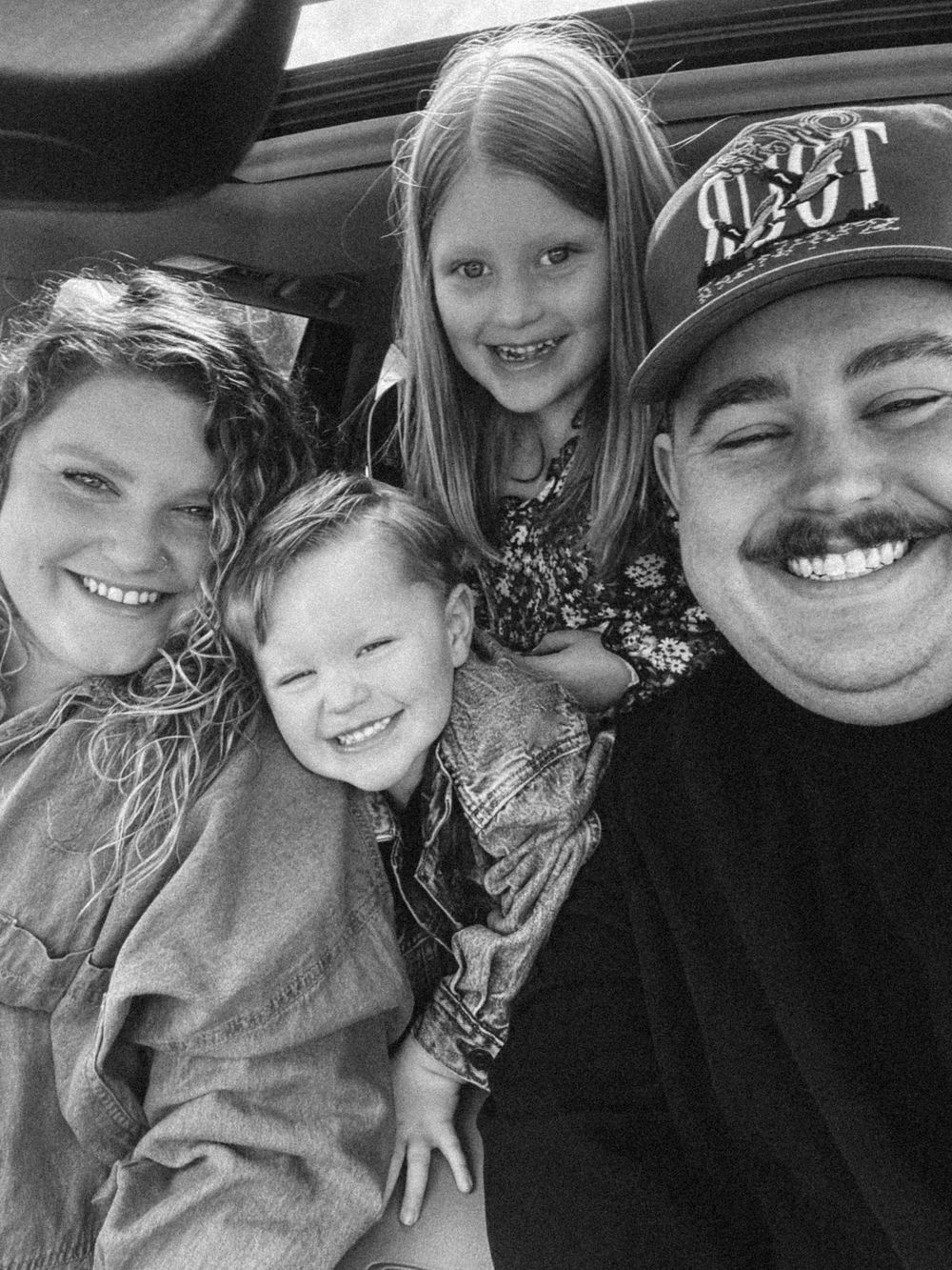 A black and white selfie of a B. Logsdon's family of four smiling together.