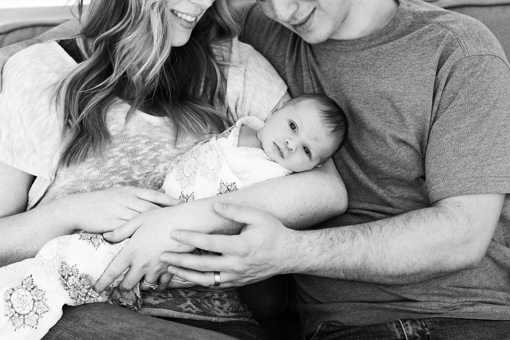 Black and white portrait of new parents snuggling with their baby.