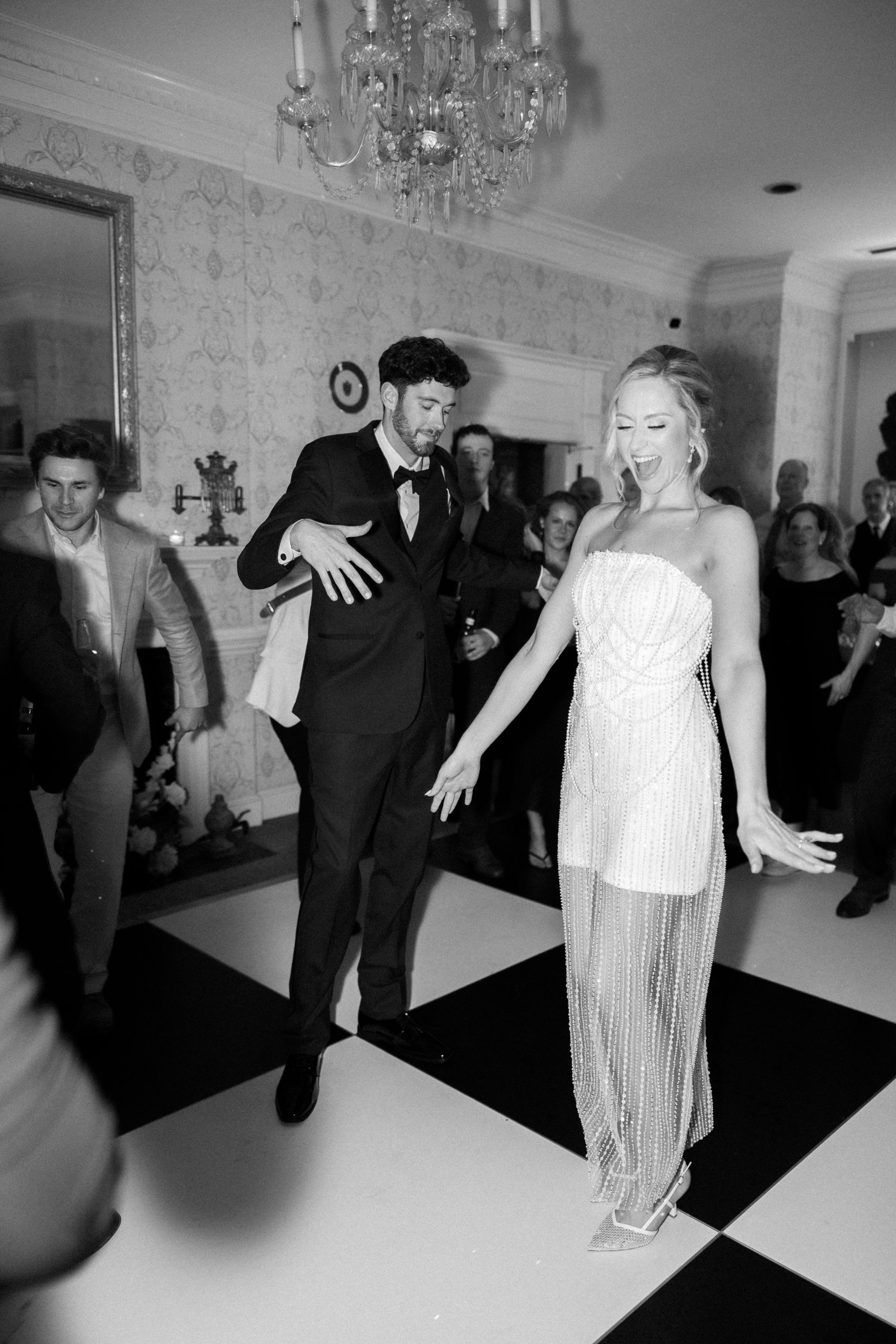 Black and white sequence of dancers performing dramatic movements on a dance floor beneath crystal chandeliers.