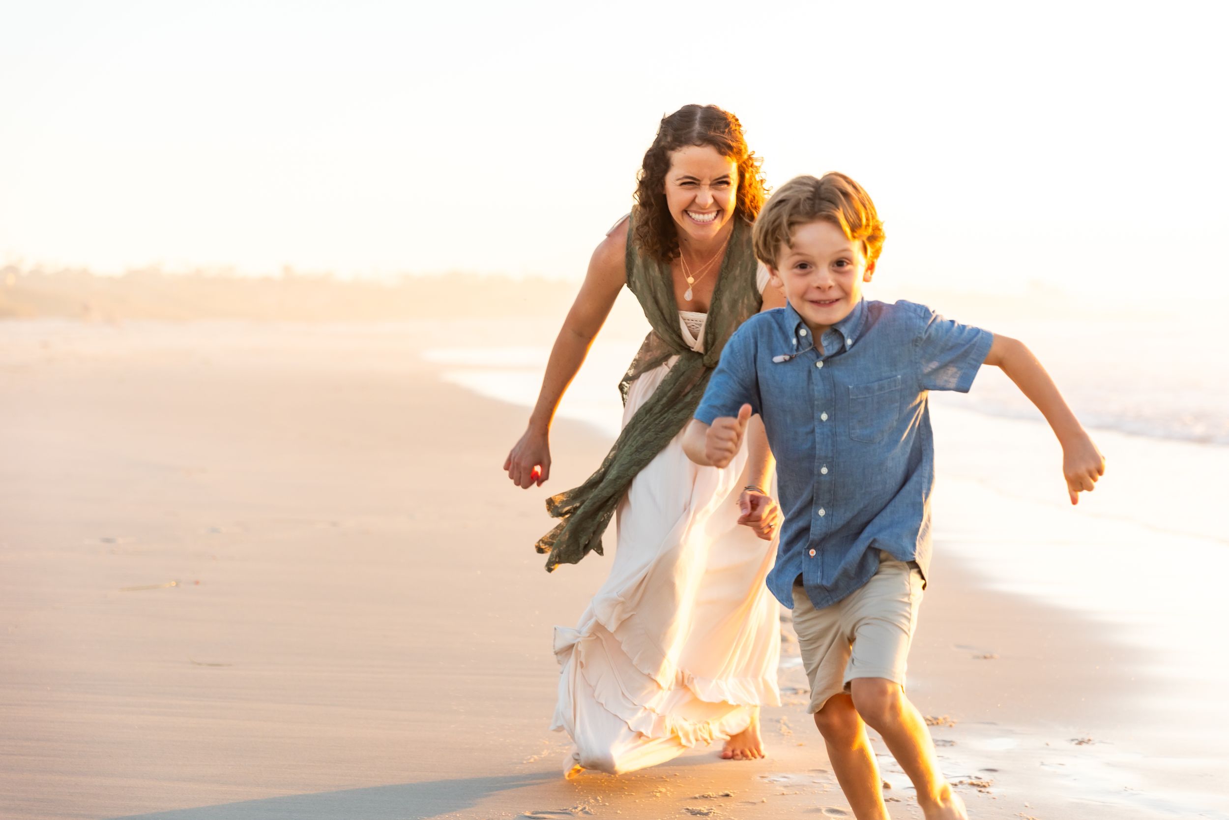 Parent and child running and laughing together on a sunny beach at sunset in Pacific Grove.
