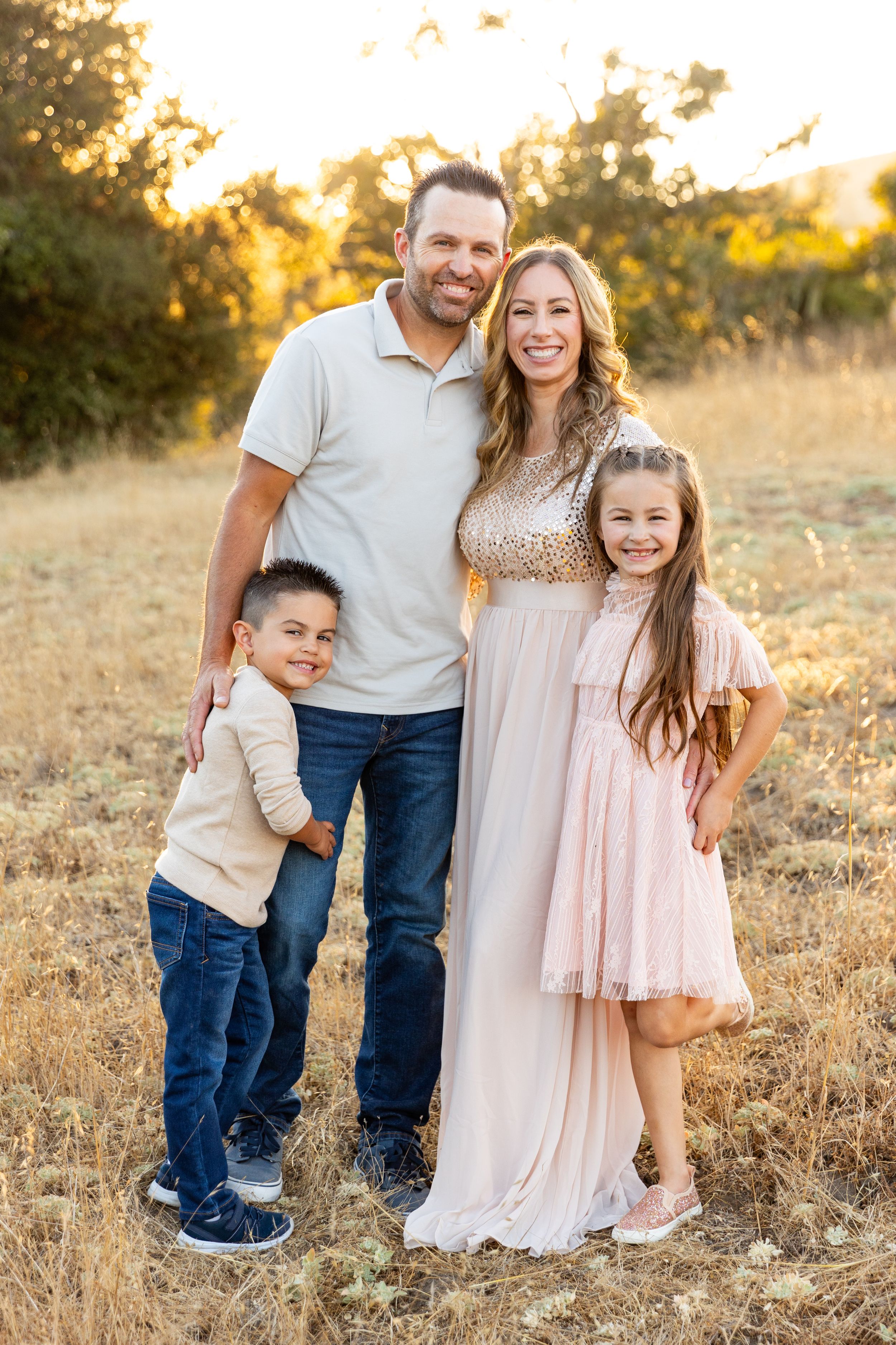 A family poses together in a field at golden hour wearing coordinating casual outfits in neutral tones for holiday card photos.