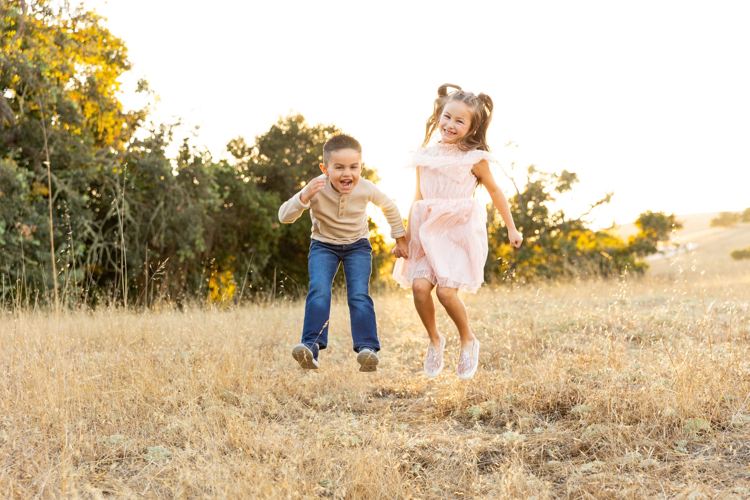 Two children playing and running together in a golden field during sunset for family pictures in Salinas.