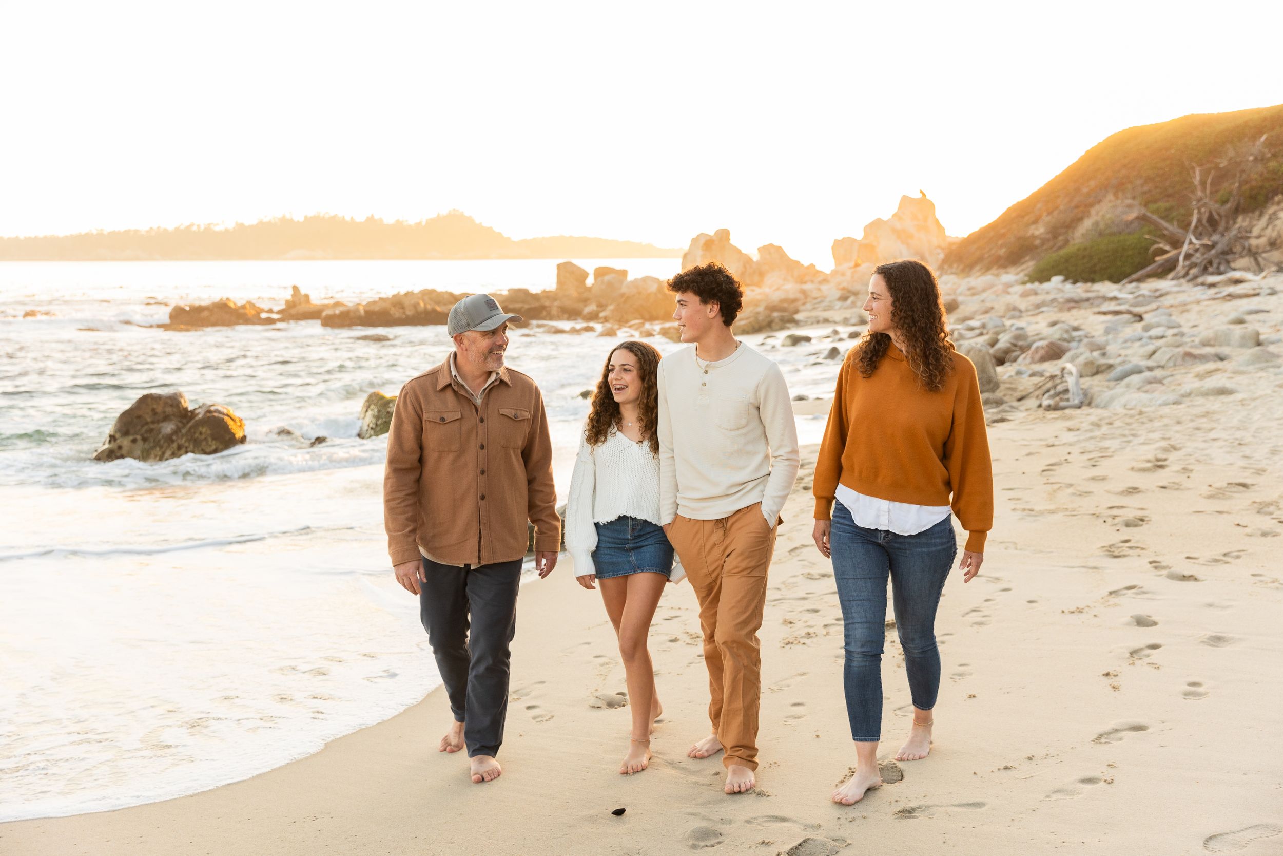A family walking together along a beach shoreline at sunset while smiling and chatting casually in Carmel.