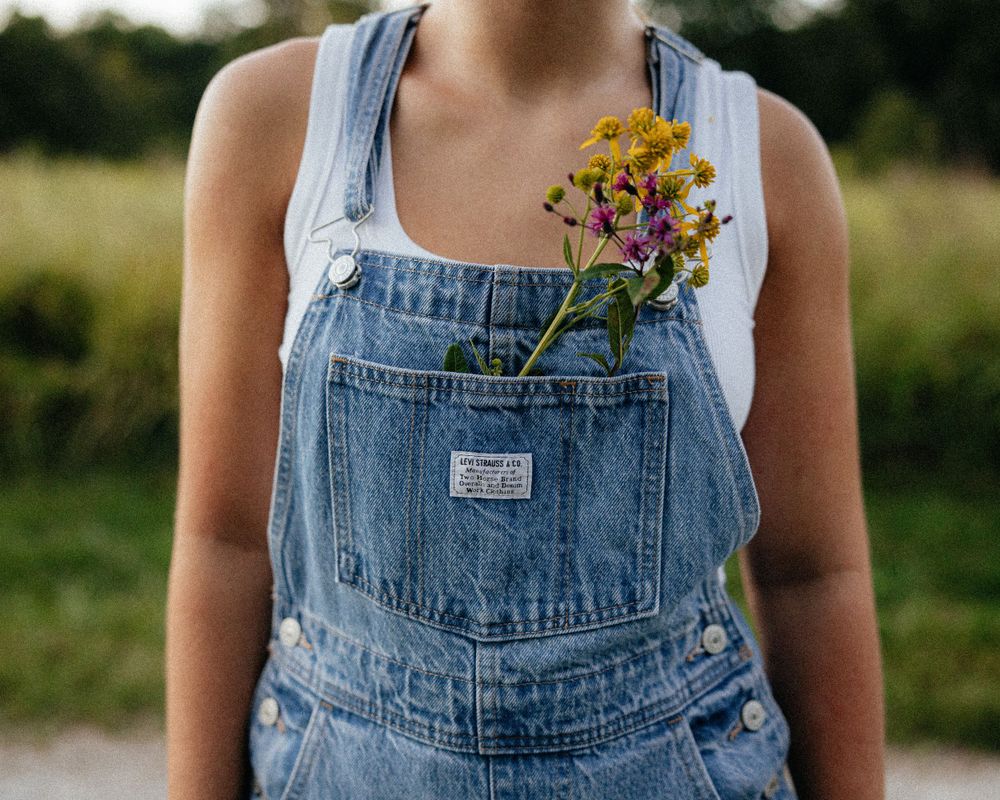 Close-up of denim overalls pocket with yellow wildflowers tucked inside.