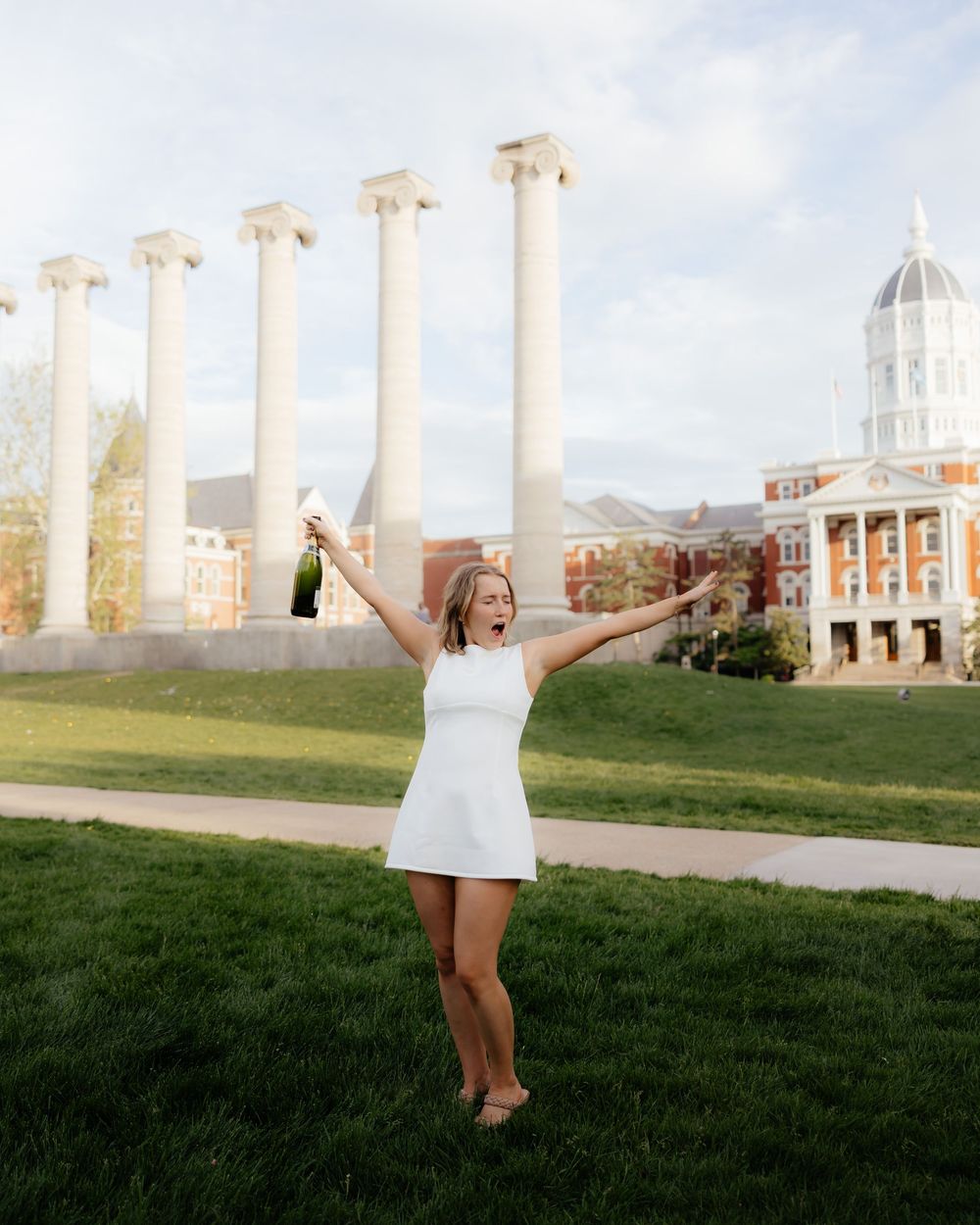 White dress photoshoot in front of iconic university columns and dome building on a sunny day.