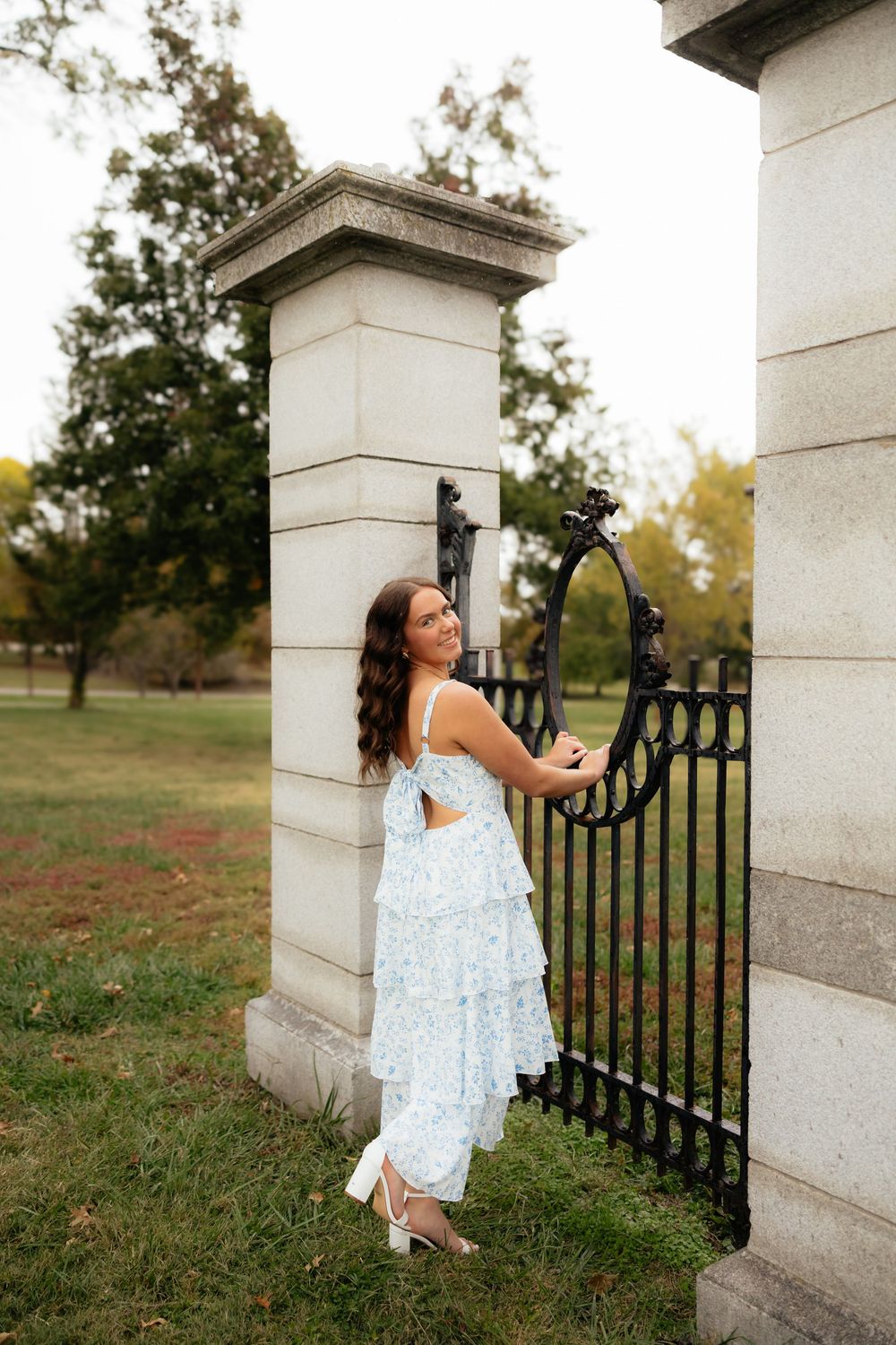 White lace dress photographed near ornate stone pillars and wrought iron fence in outdoor setting.