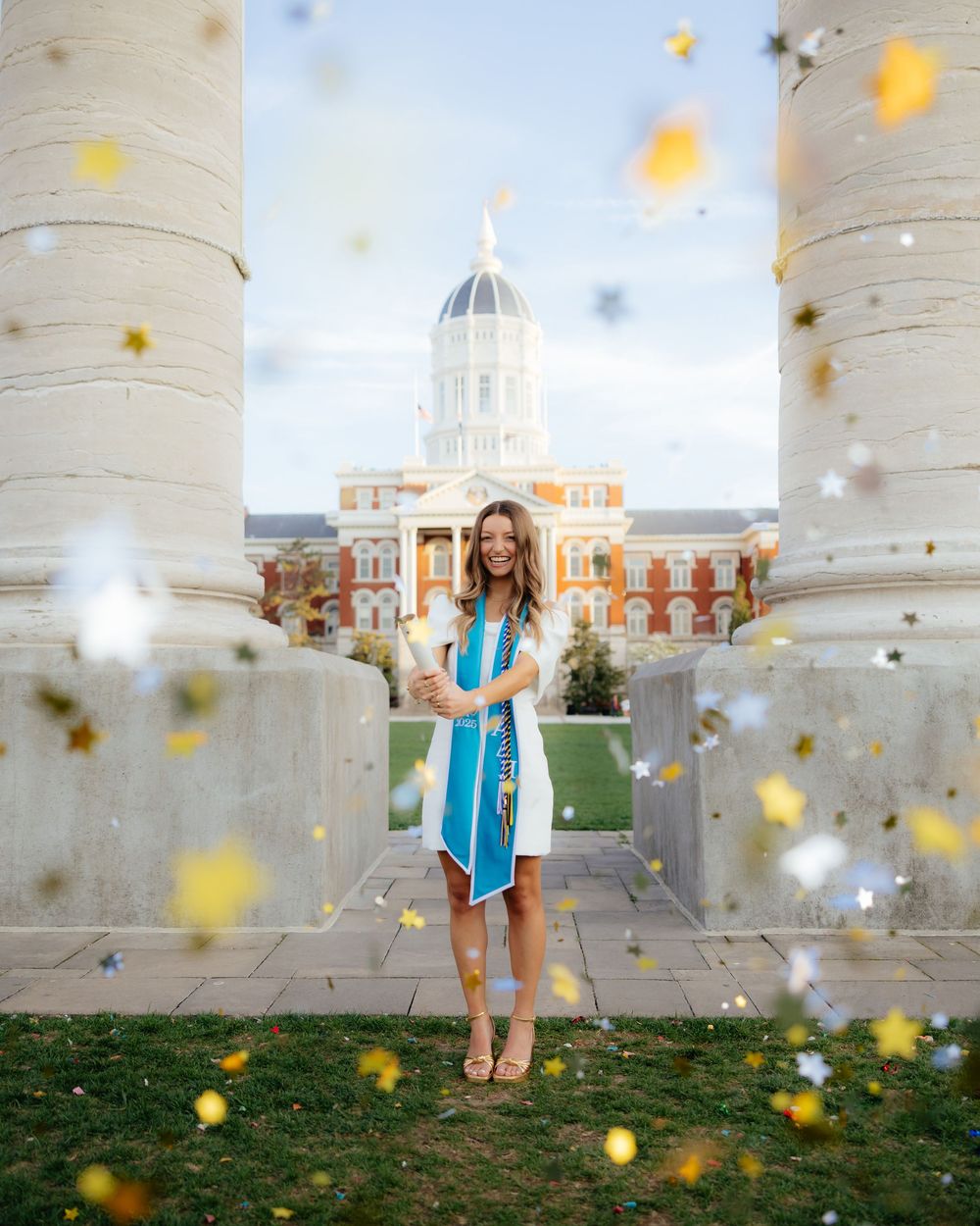 Yellow confetti falls around white columns with a domed building visible in the background.