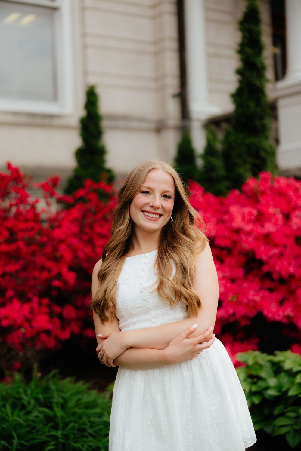 White dress against vibrant red azalea bushes in a springtime portrait setting.