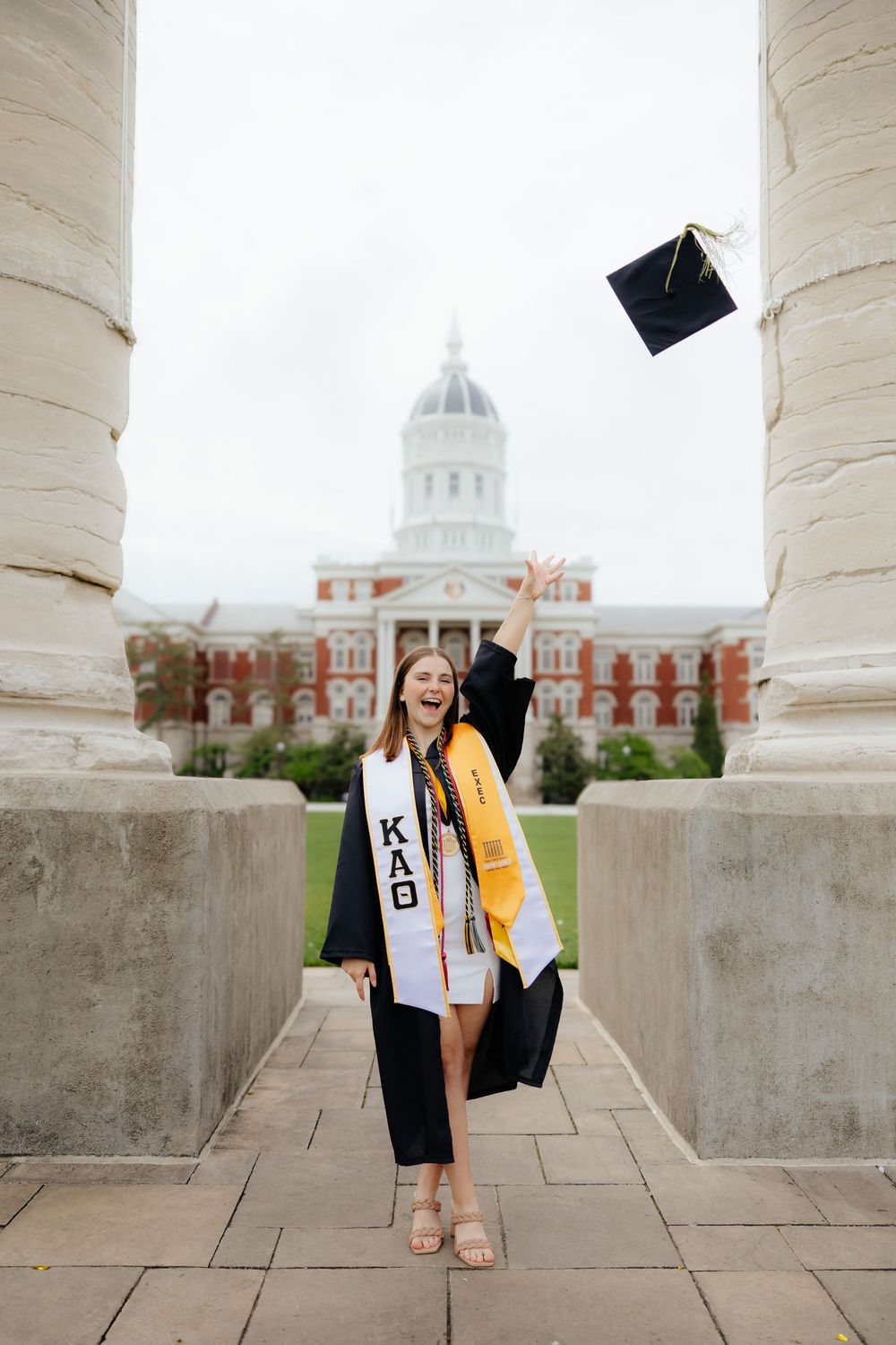 Graduate celebrates with cap toss in front of columned university building.