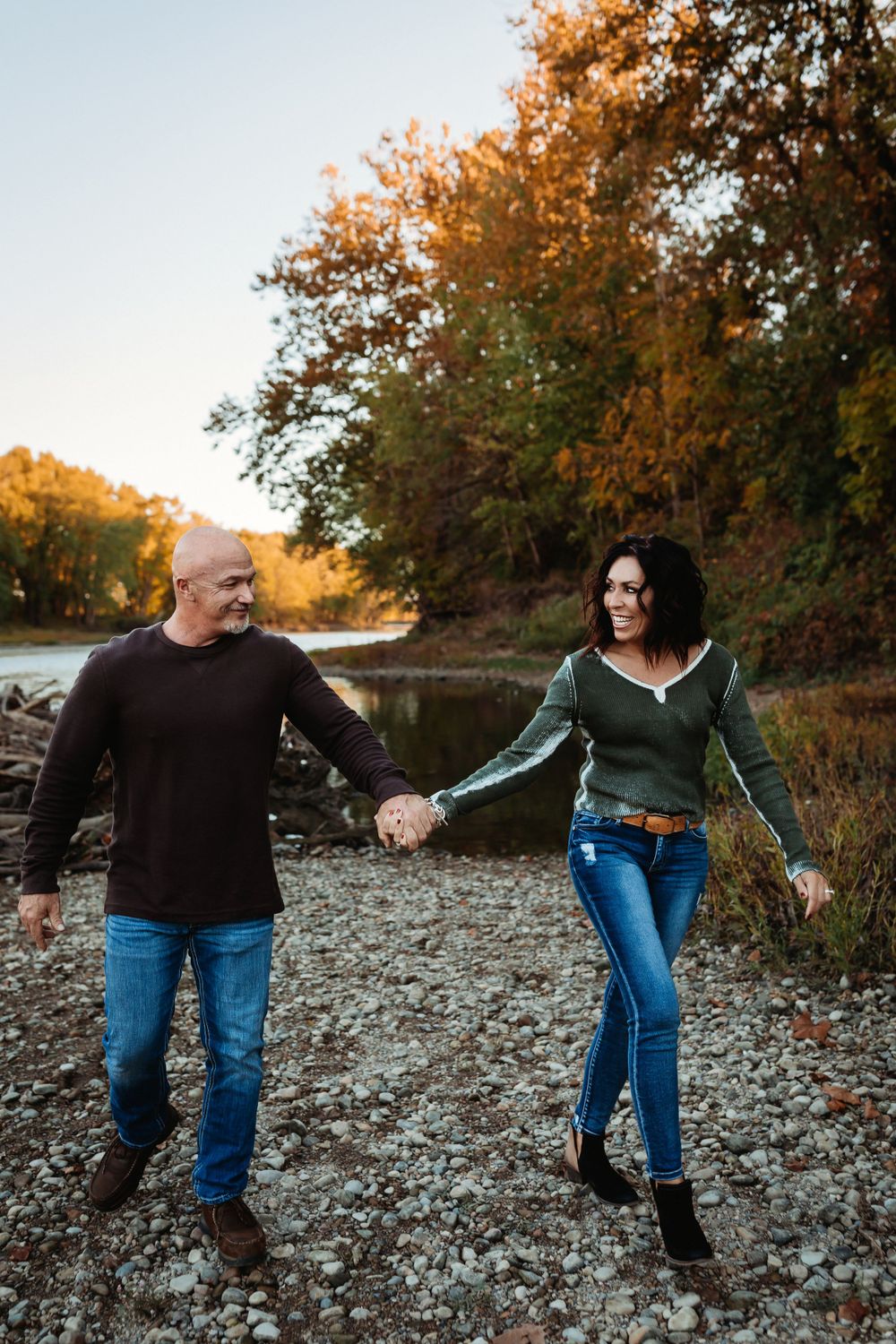 Couple holding hands and walking on rocky terrain during golden autumn sunset.