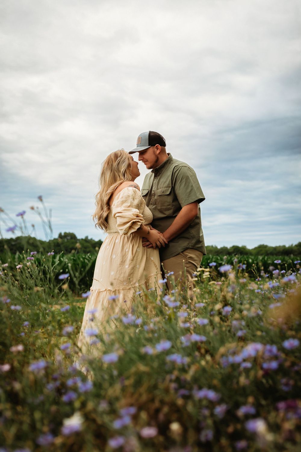 A couple shares a romantic moment in a blooming wildflower field under cloudy skies.