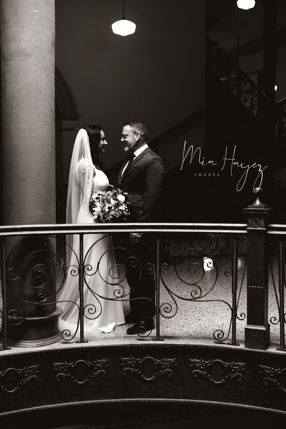 Dramatic black and white wedding photos on ornate balcony with elegant lighting.