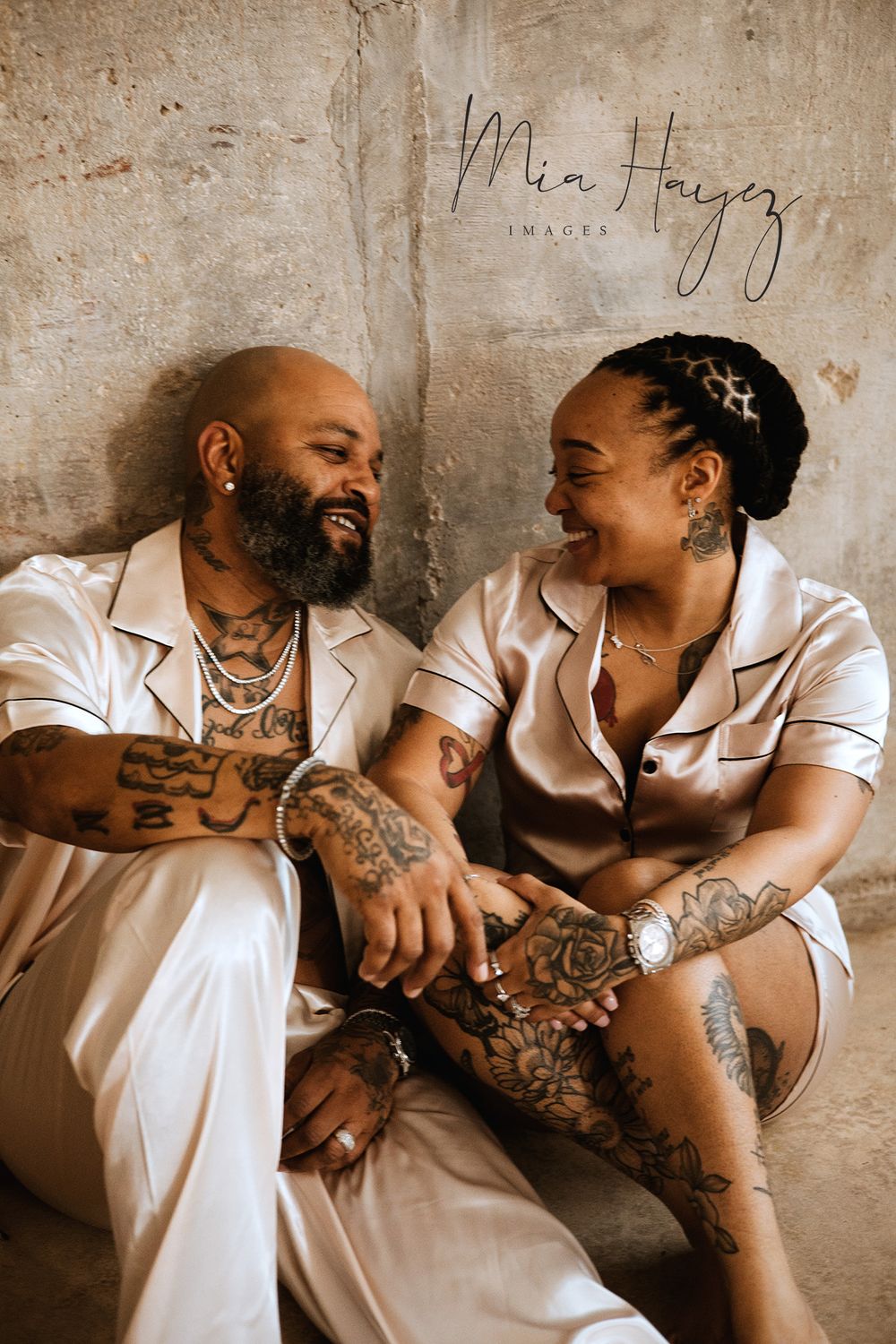Intimate couple photoshoot with matching white outfits against a textured concrete wall.