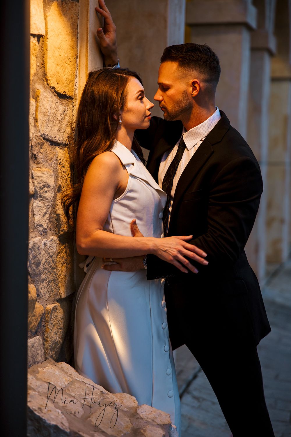 Elegant engagement photos showing couple in formal wear against stone wall backdrop.