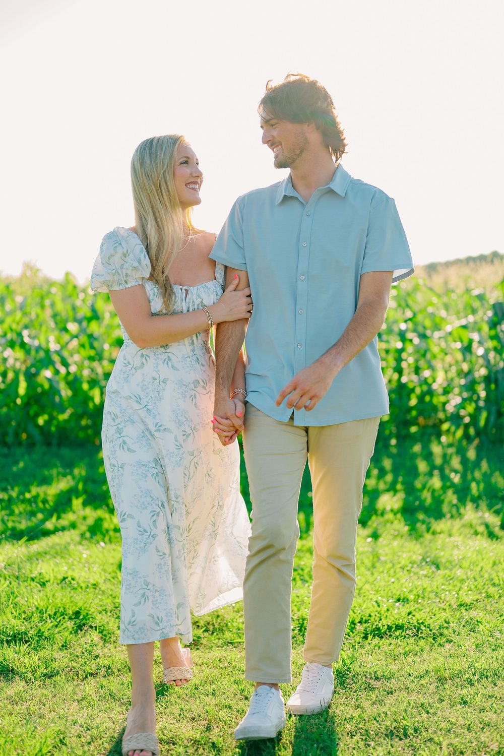A couple walks together through a sunny vineyard wearing light summer clothing.