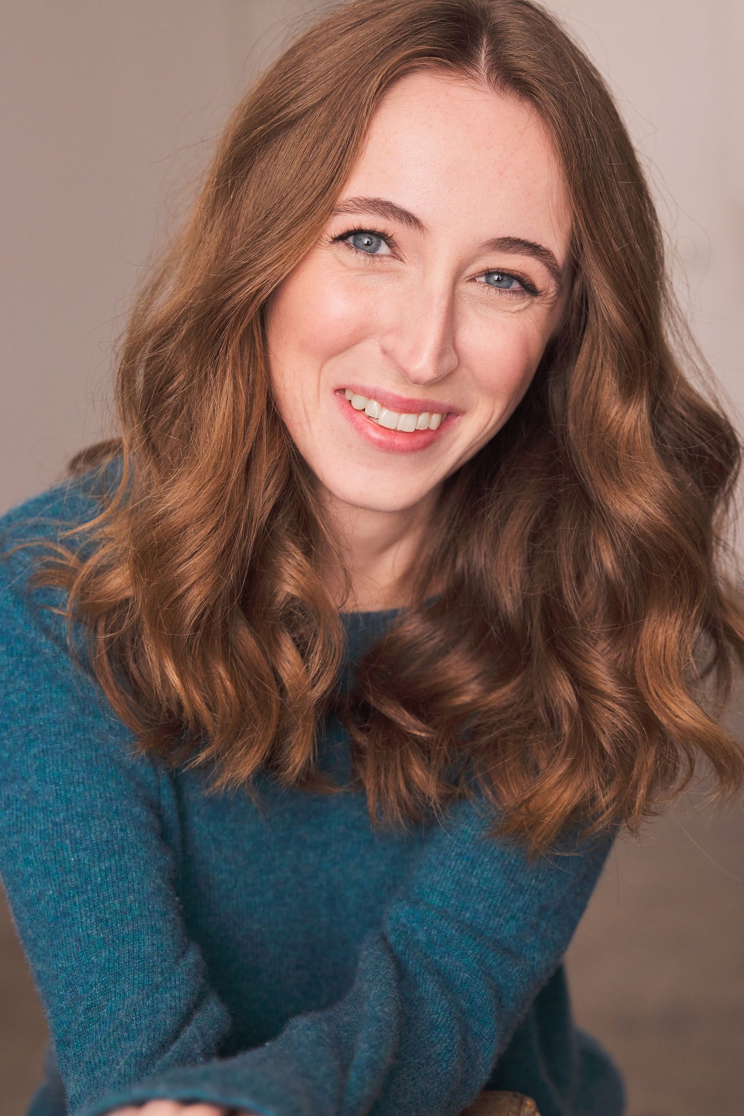 Professional actor headshot Sophia Goodin with medium length hair in a yellow top and denim jacket against a blue background.