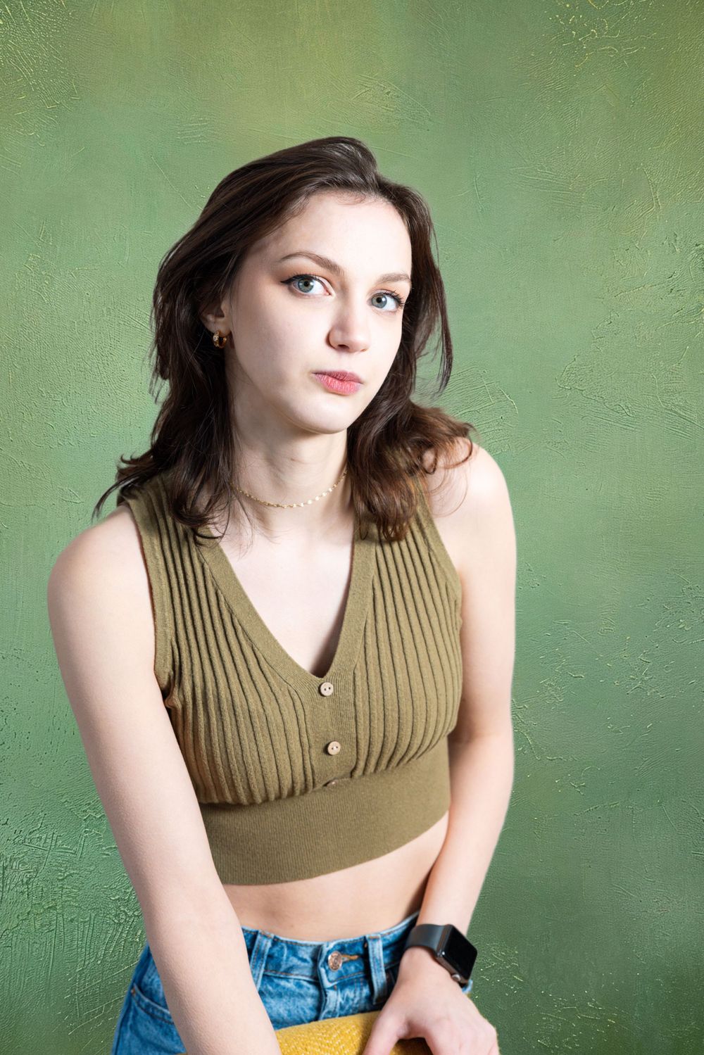 A young brunette woman in a green ribbed crop top and jeans poses against a green background.